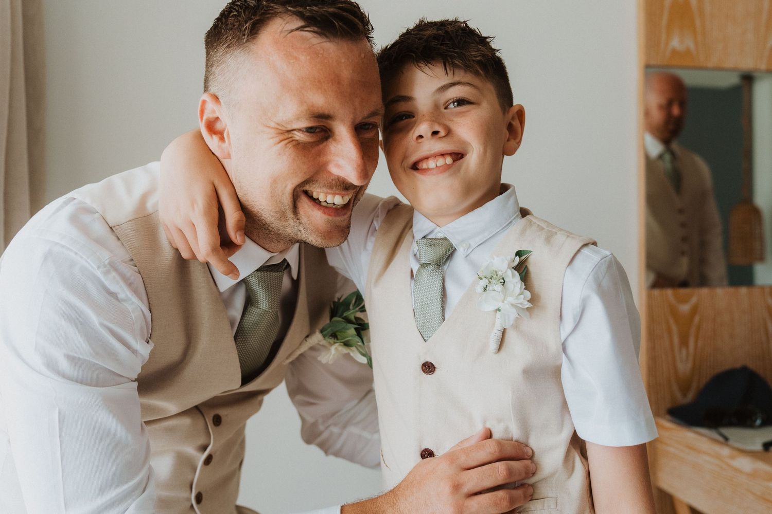 A heartwarming candid moment between two people wearing white shirts and boutonnières at a formal event.