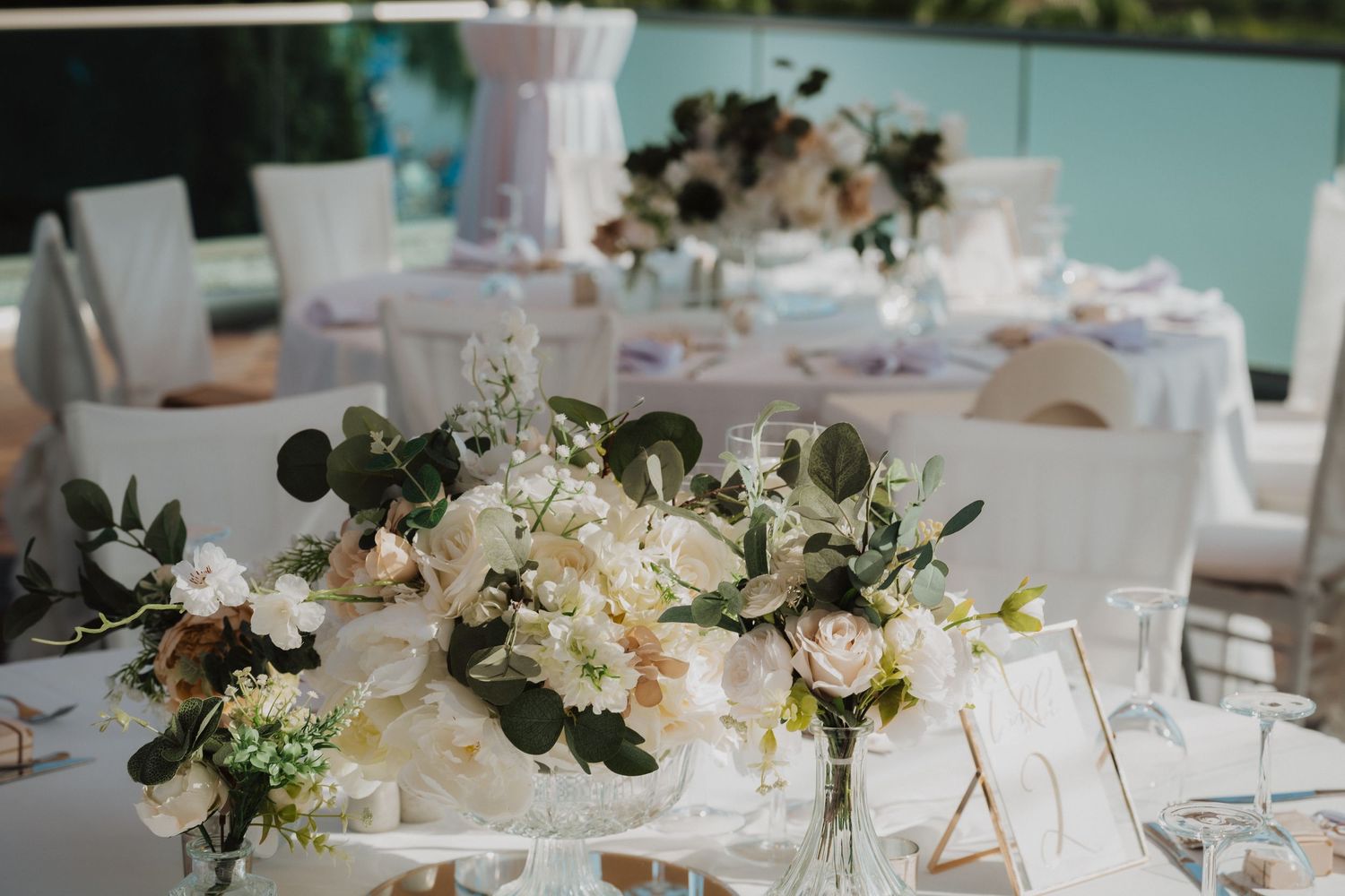 Romantic table setting with white roses, eucalyptus and crystal vases on white linens.