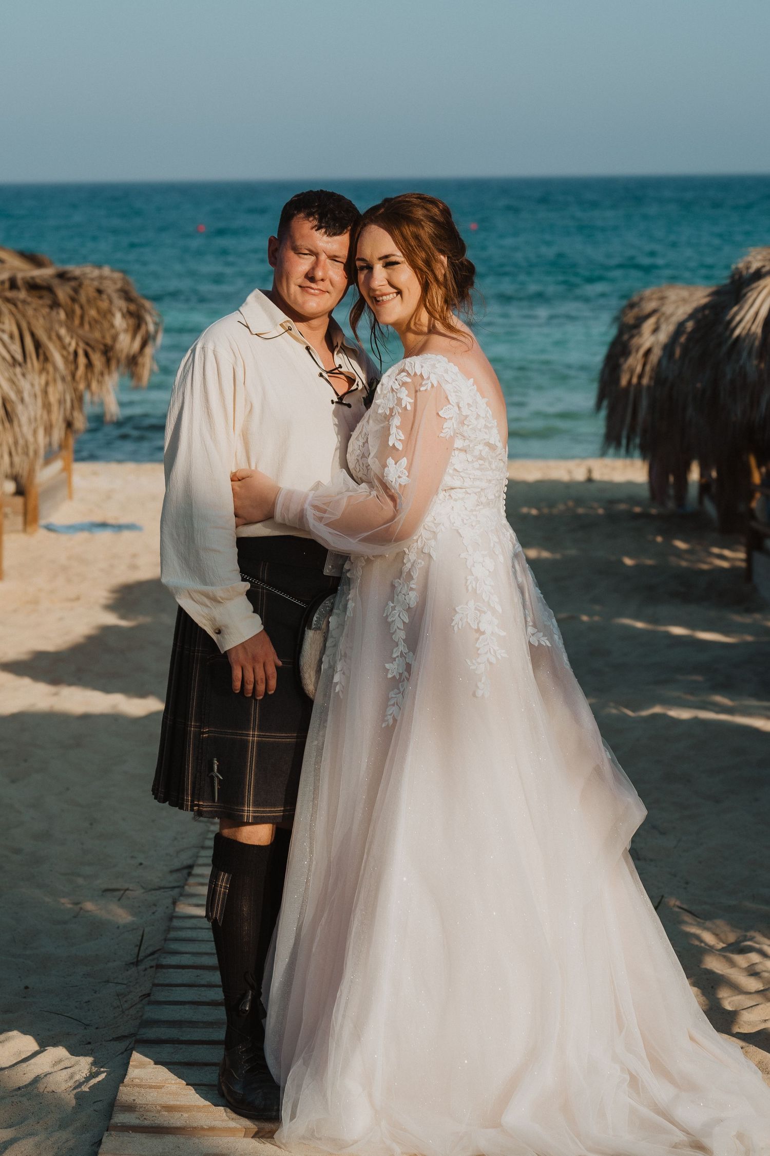 A joyful beach wedding moment captured between thatched umbrellas with ocean views.
