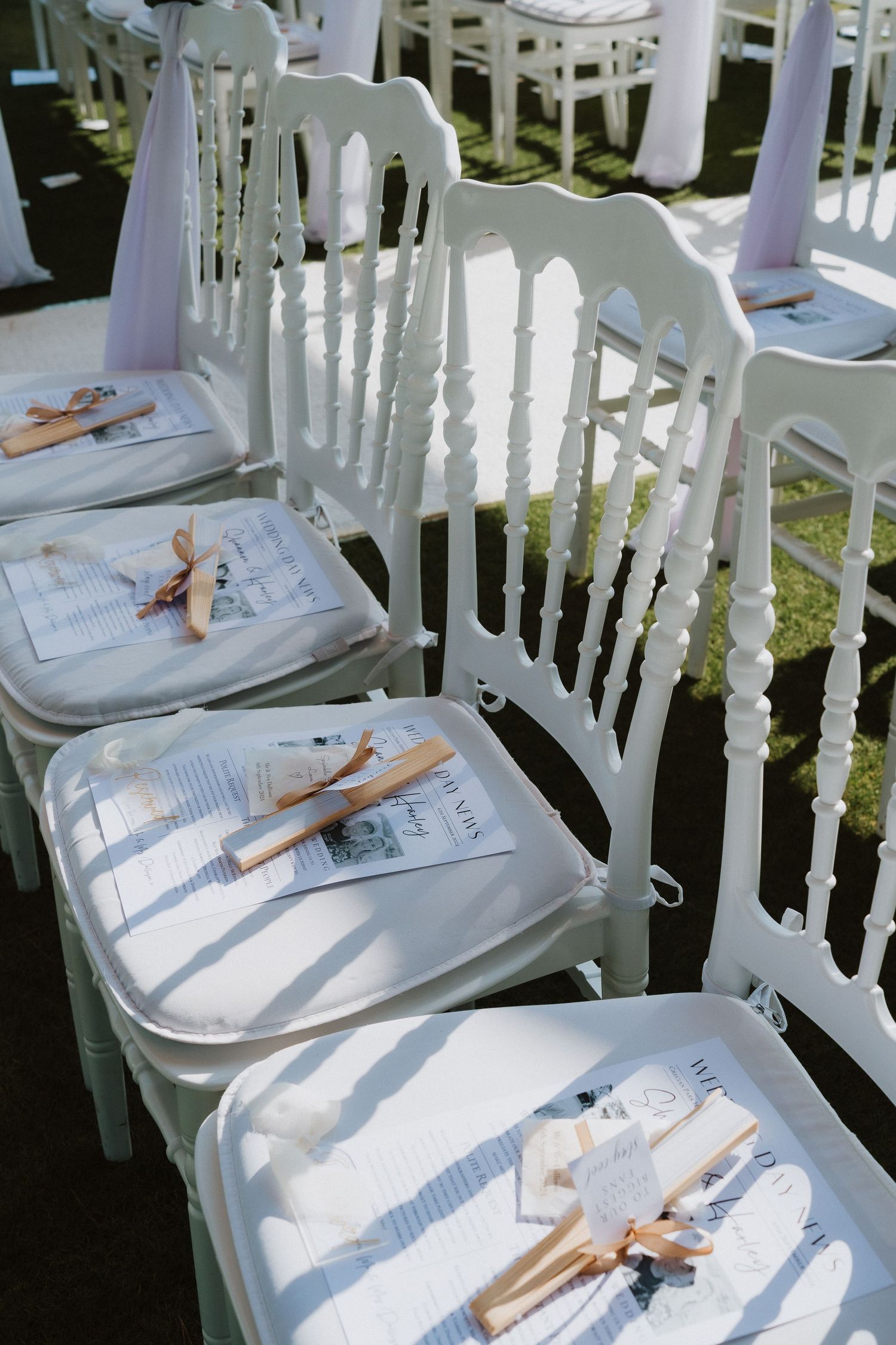 White wedding chairs arranged in rows with program booklets and fans placed on the seats for guests.