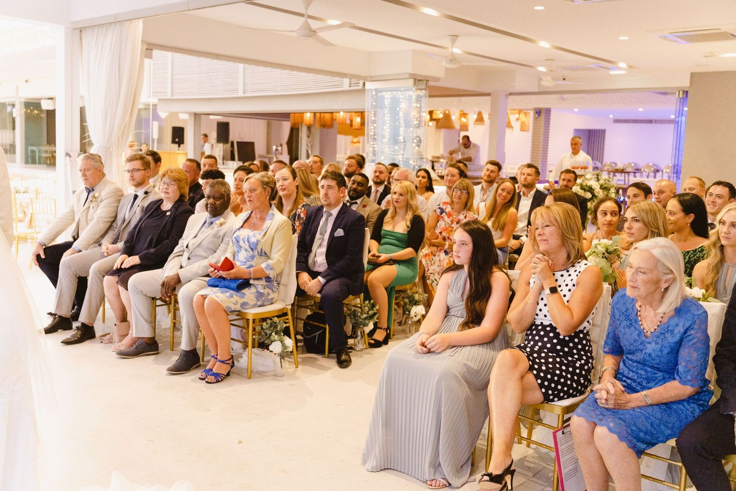 Well-dressed wedding guests seated in rows at an elegant indoor ceremony venue.
