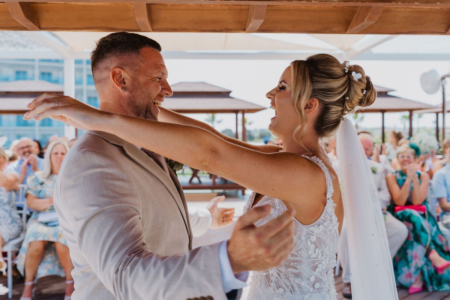 A couple shares a joyful dance moment during their wedding celebration, surrounded by wooden beams and natural light.