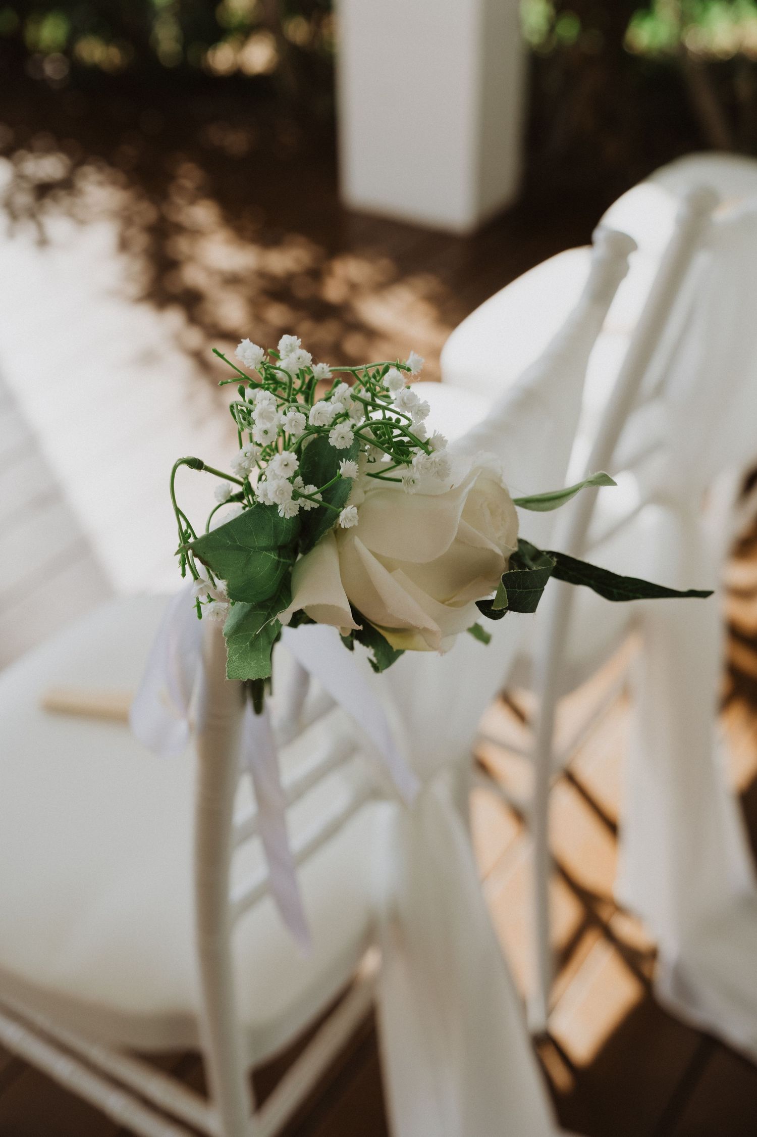 White floral decorations adorn chairs at an elegant wedding ceremony setup.