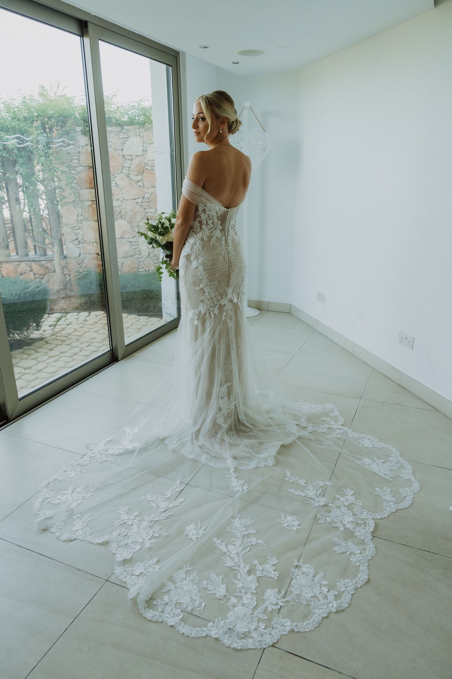 Full-length shots of a bride in a lace wedding gown with cathedral train near large windows.