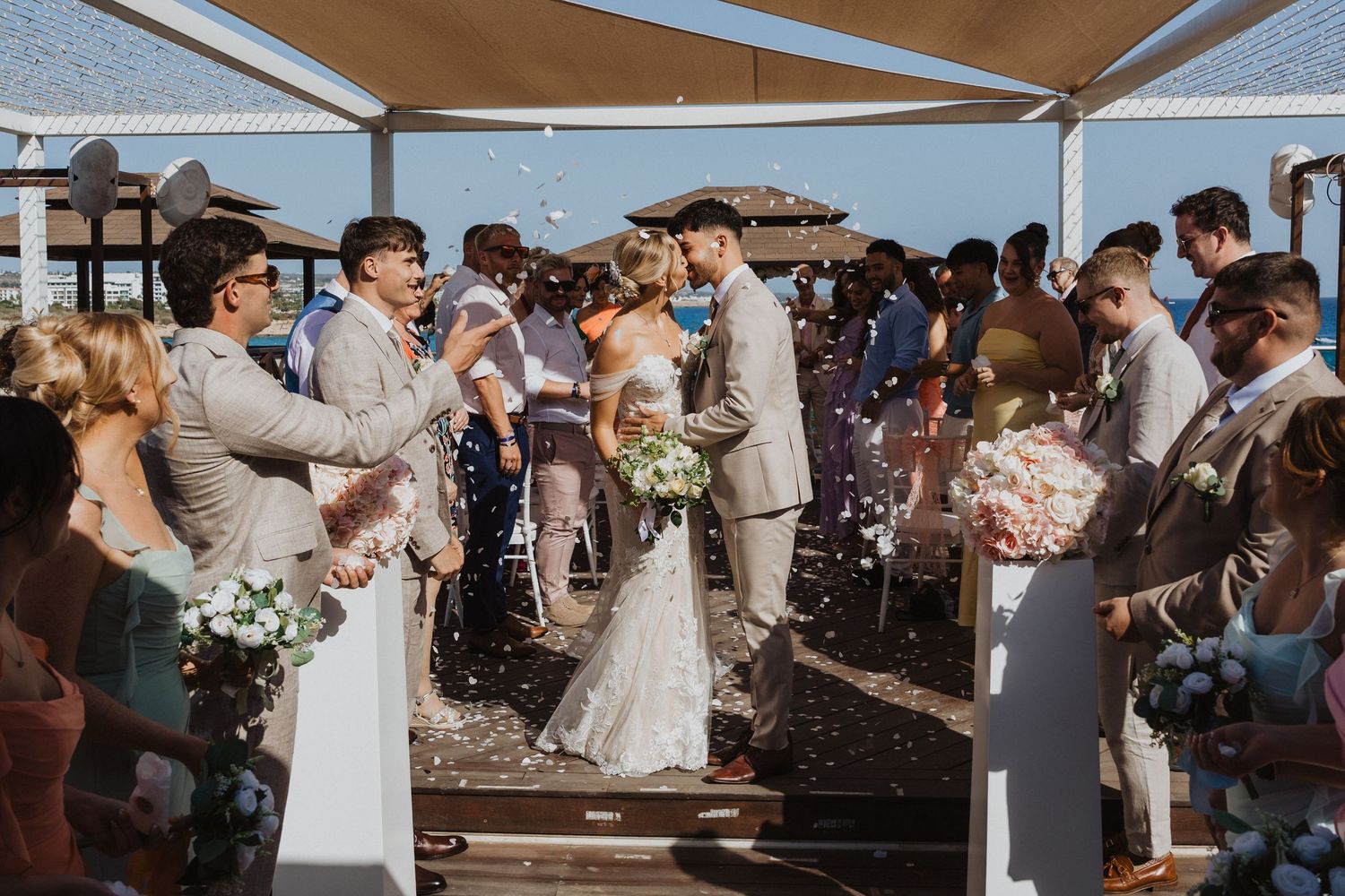 Outdoor wedding reception with guests celebrating under covered seaside venue.