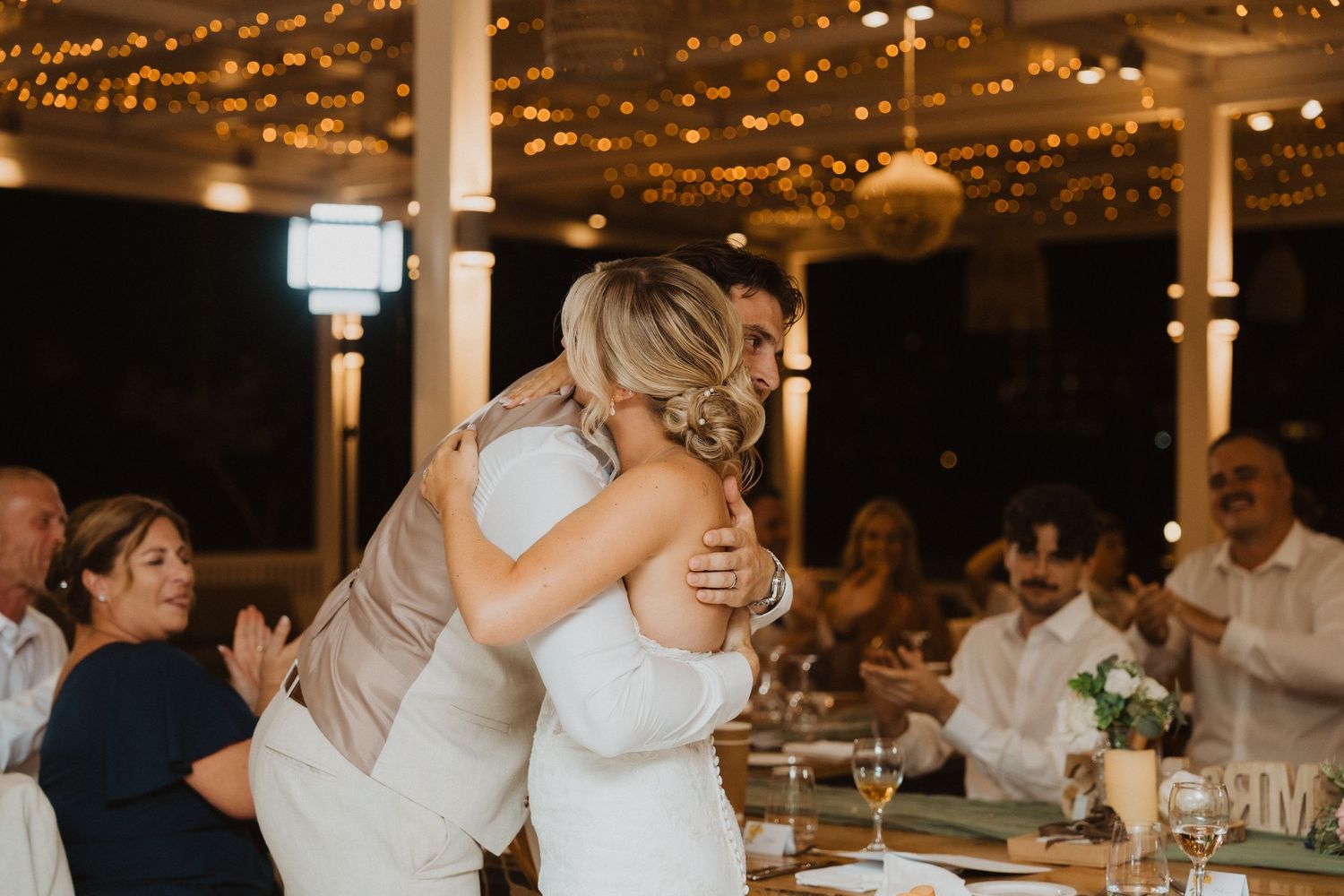 Wedding reception guests dancing and mingling under warm string lights in an elegant indoor venue.