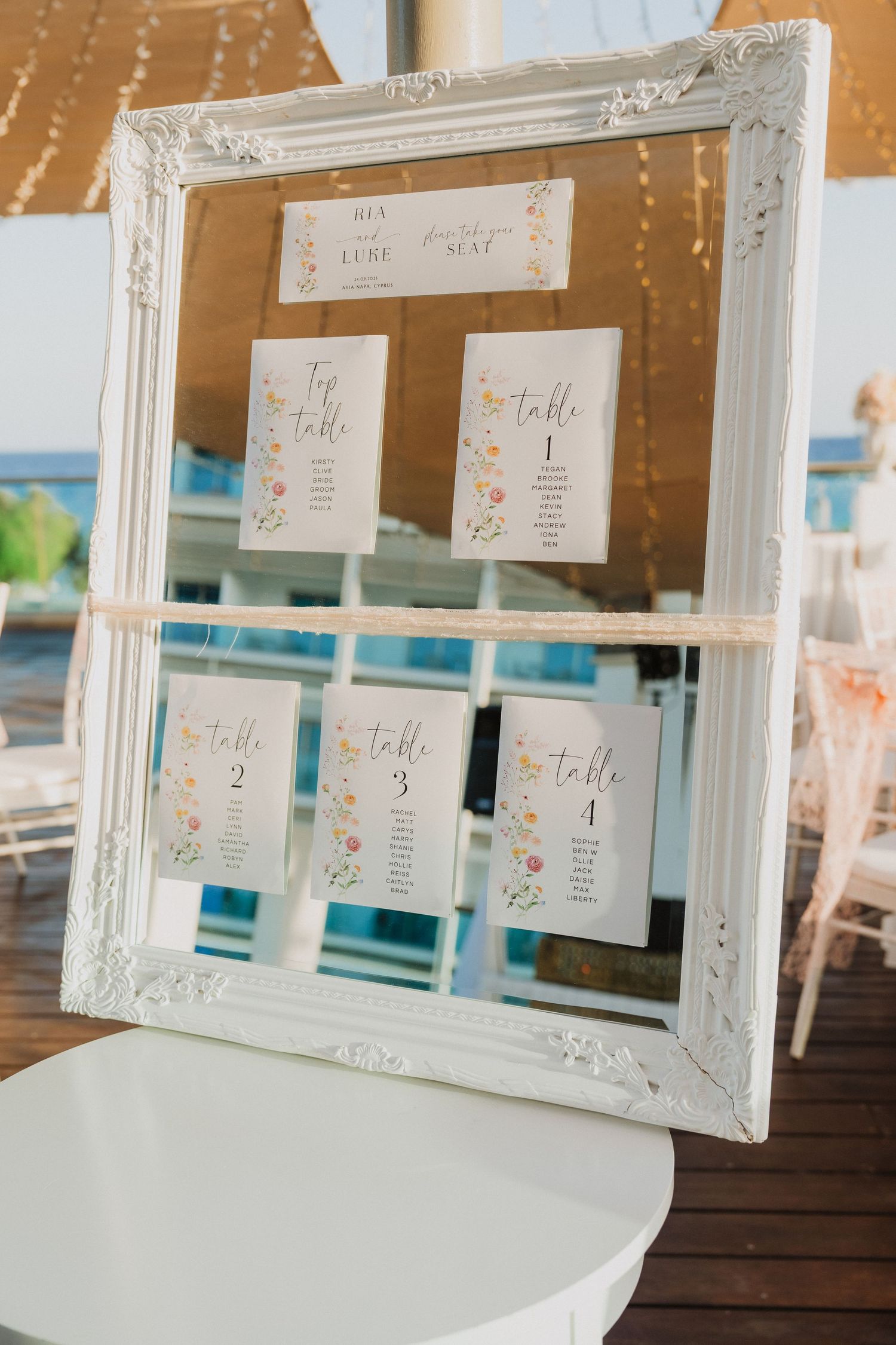 Ornate white frames display wedding seating arrangements with delicate floral designs.