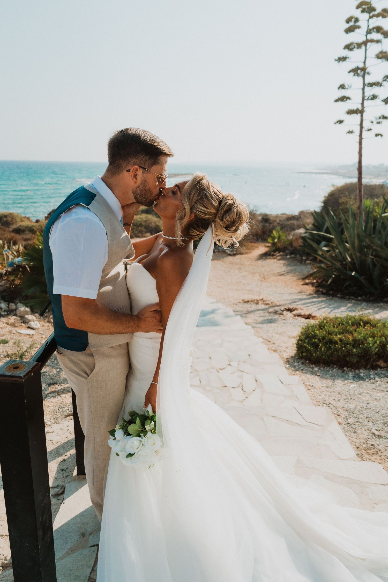 Bride and groom sharing a romantic kiss at a coastal wedding venue with ocean views and flowing white veil.