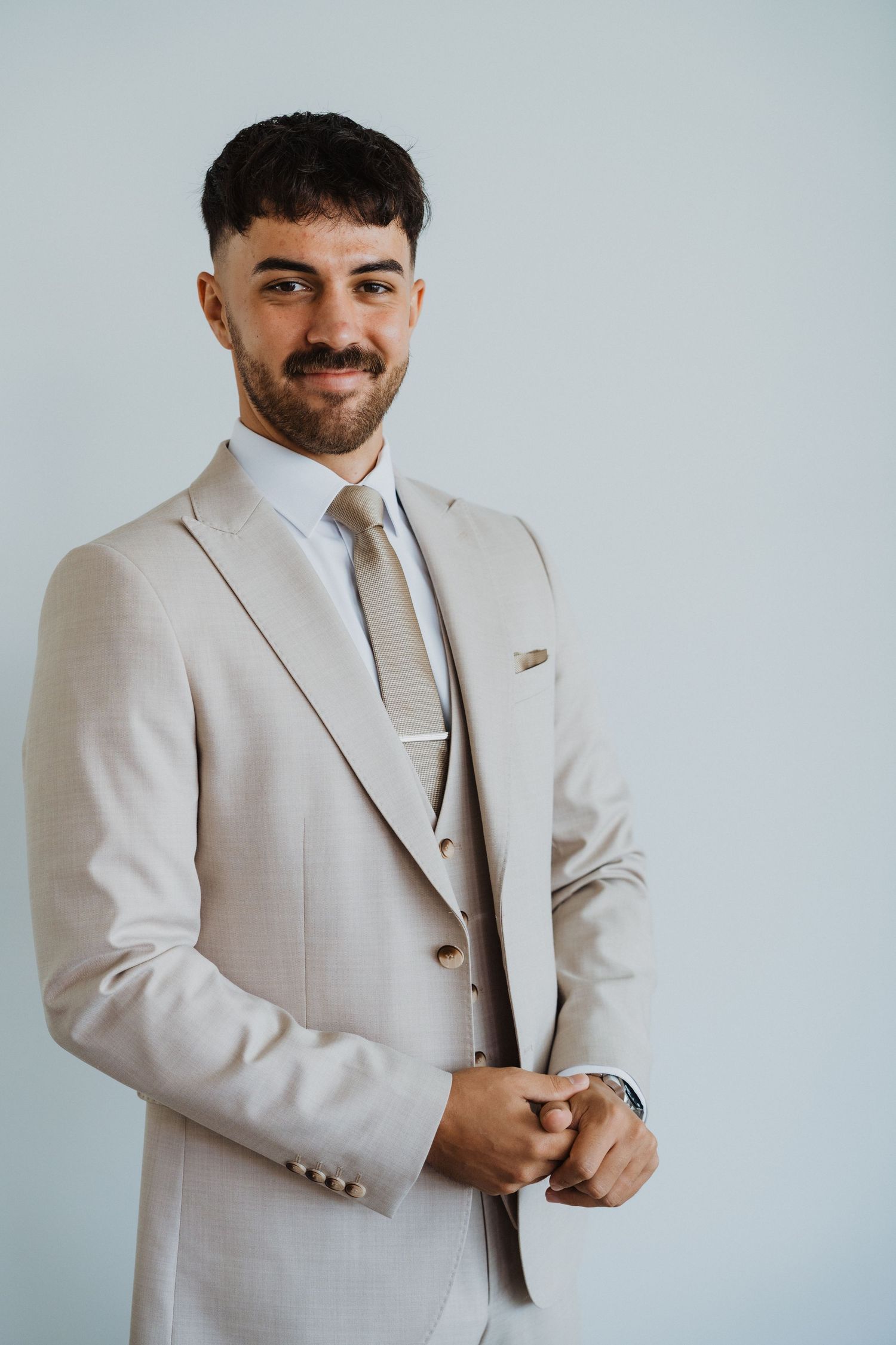 Elegant groom in light beige suit preparing for wedding ceremony.