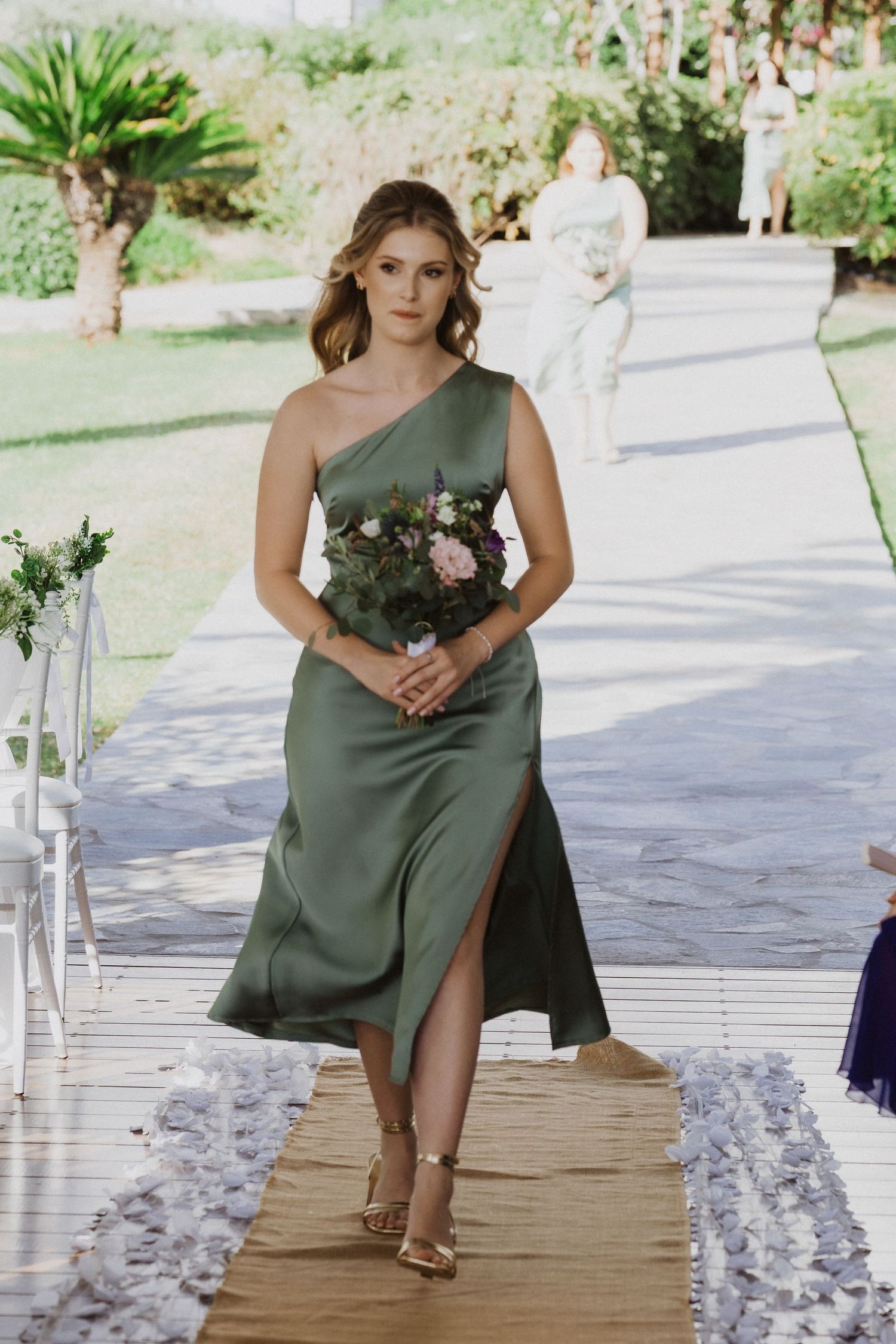 Bridesmaid in sage green dress poses on outdoor deck with floral decorations.