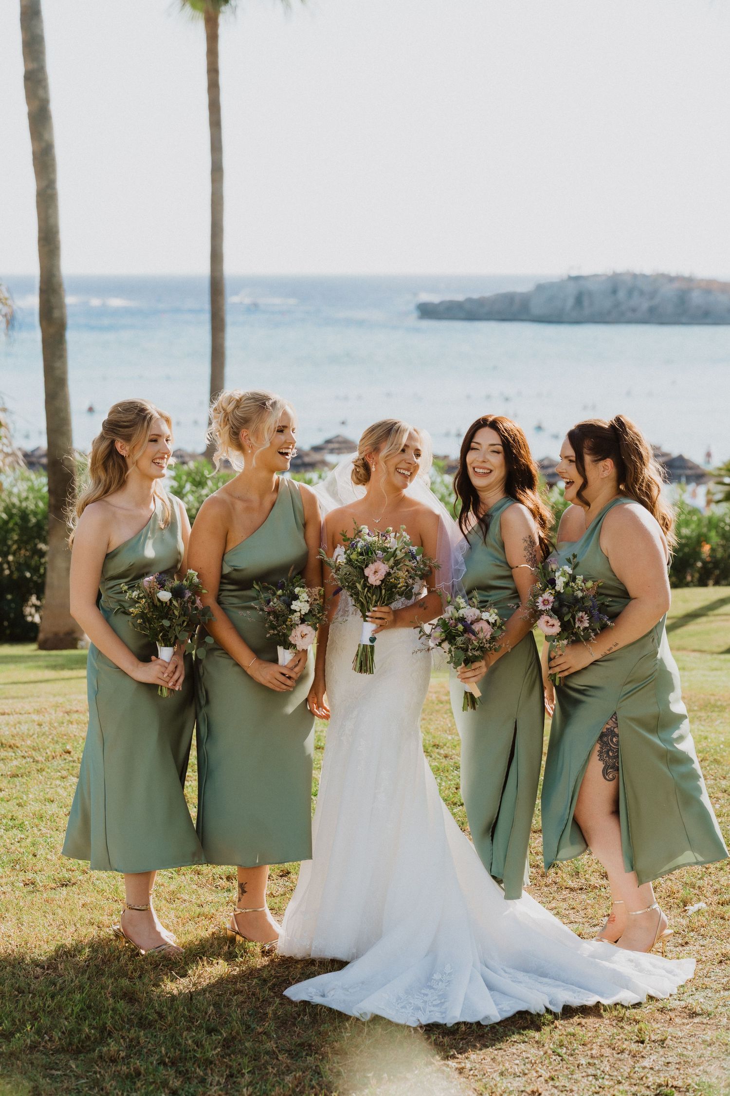 Wedding party in mint green dresses and white gown gather for photos on grassy lawn with palm trees.