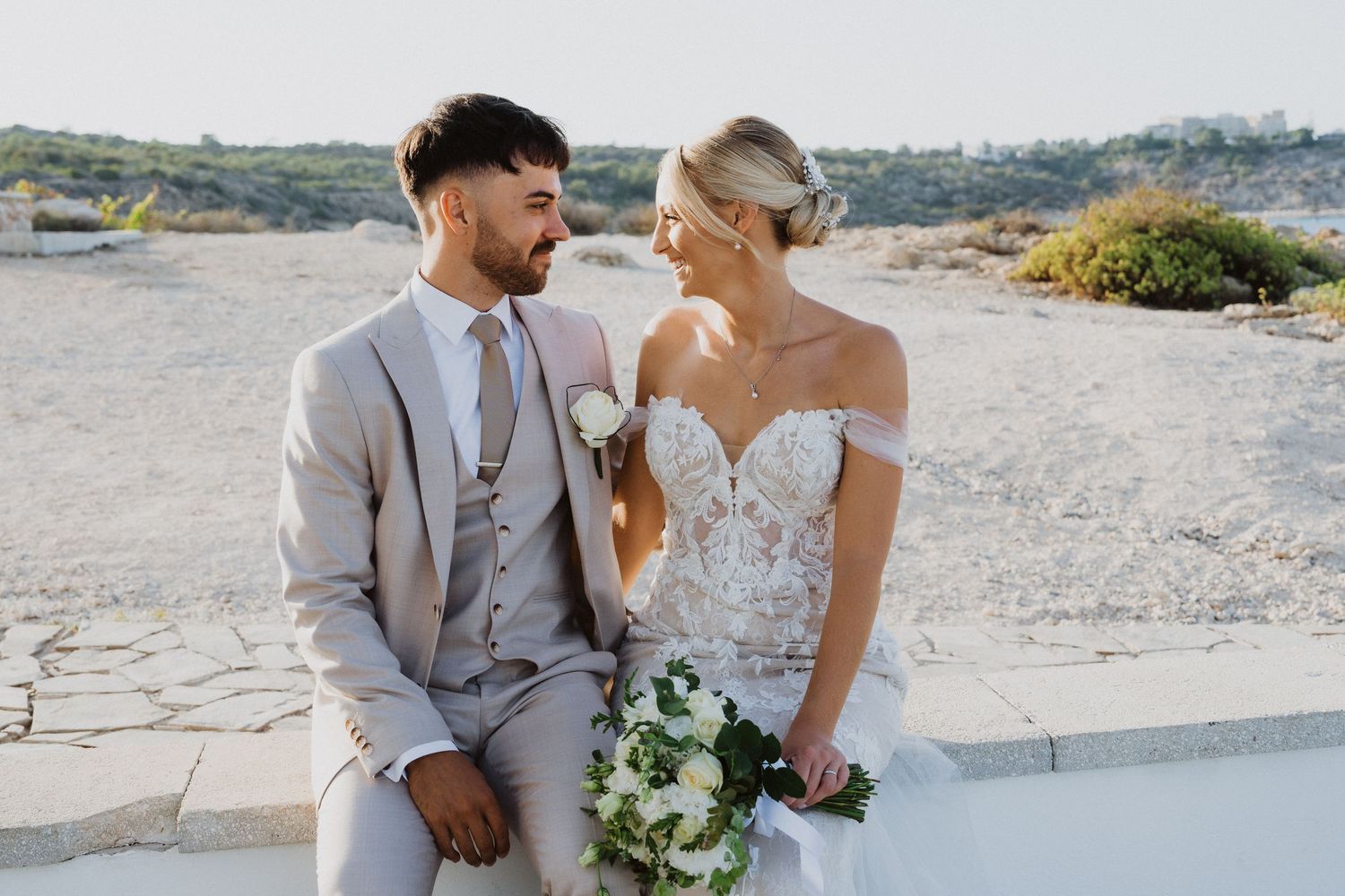 A romantic wedding photoshoot against a Mediterranean coastal backdrop in soft natural lighting.