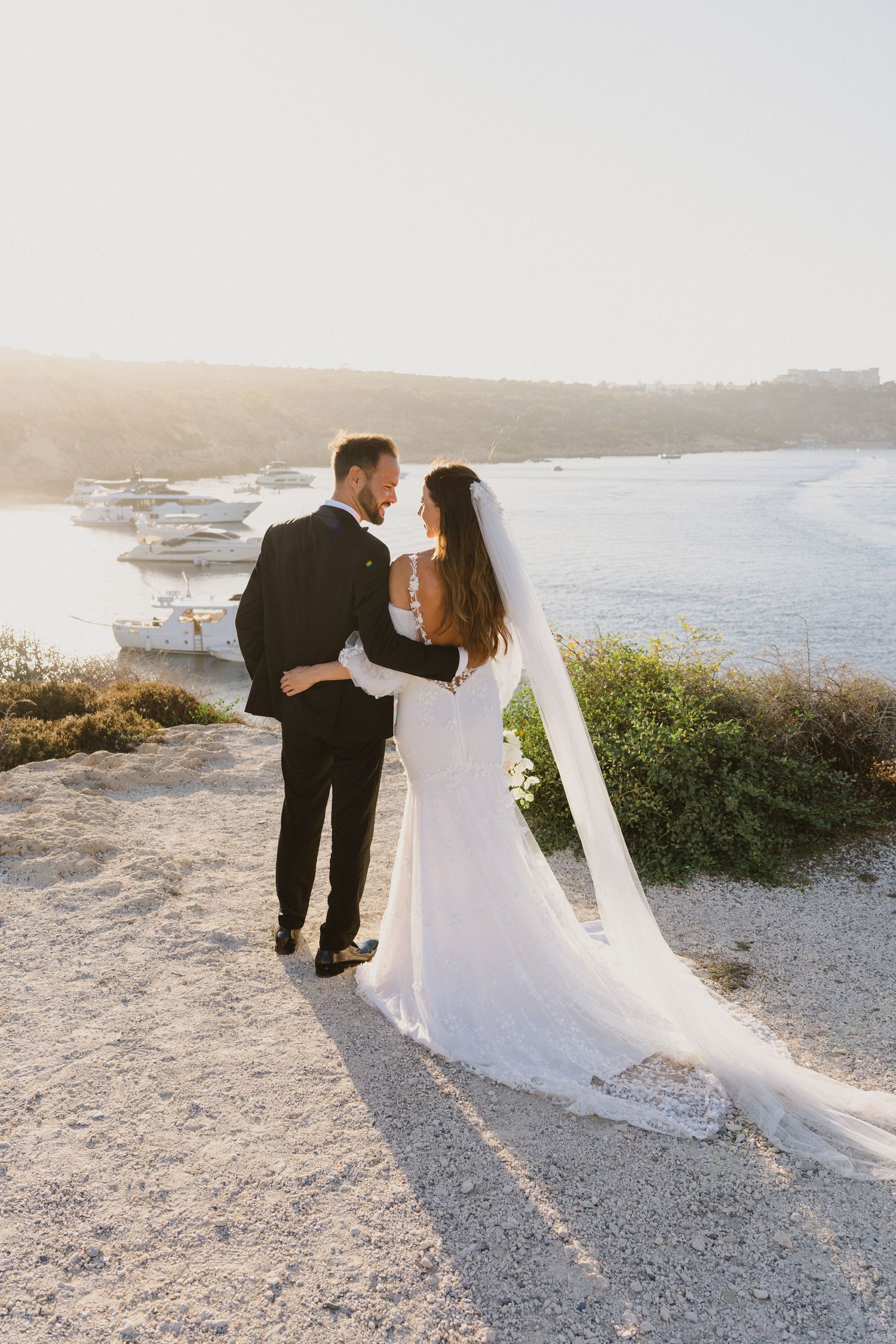 Couple embraces on coastal cliff path during golden hour with ocean views.