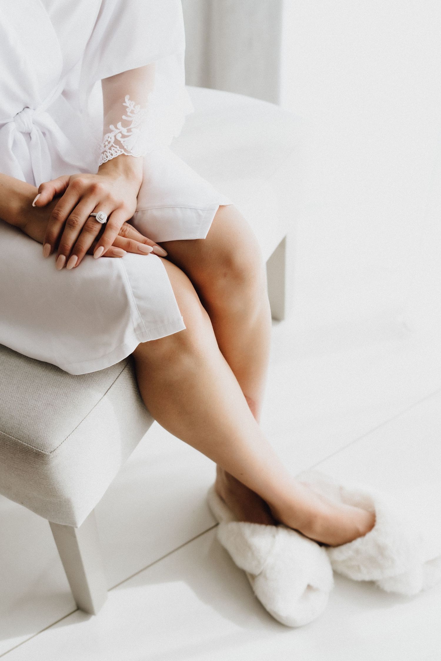Close up of hands and legs showing delicate lace details on white robe and cozy slippers.
