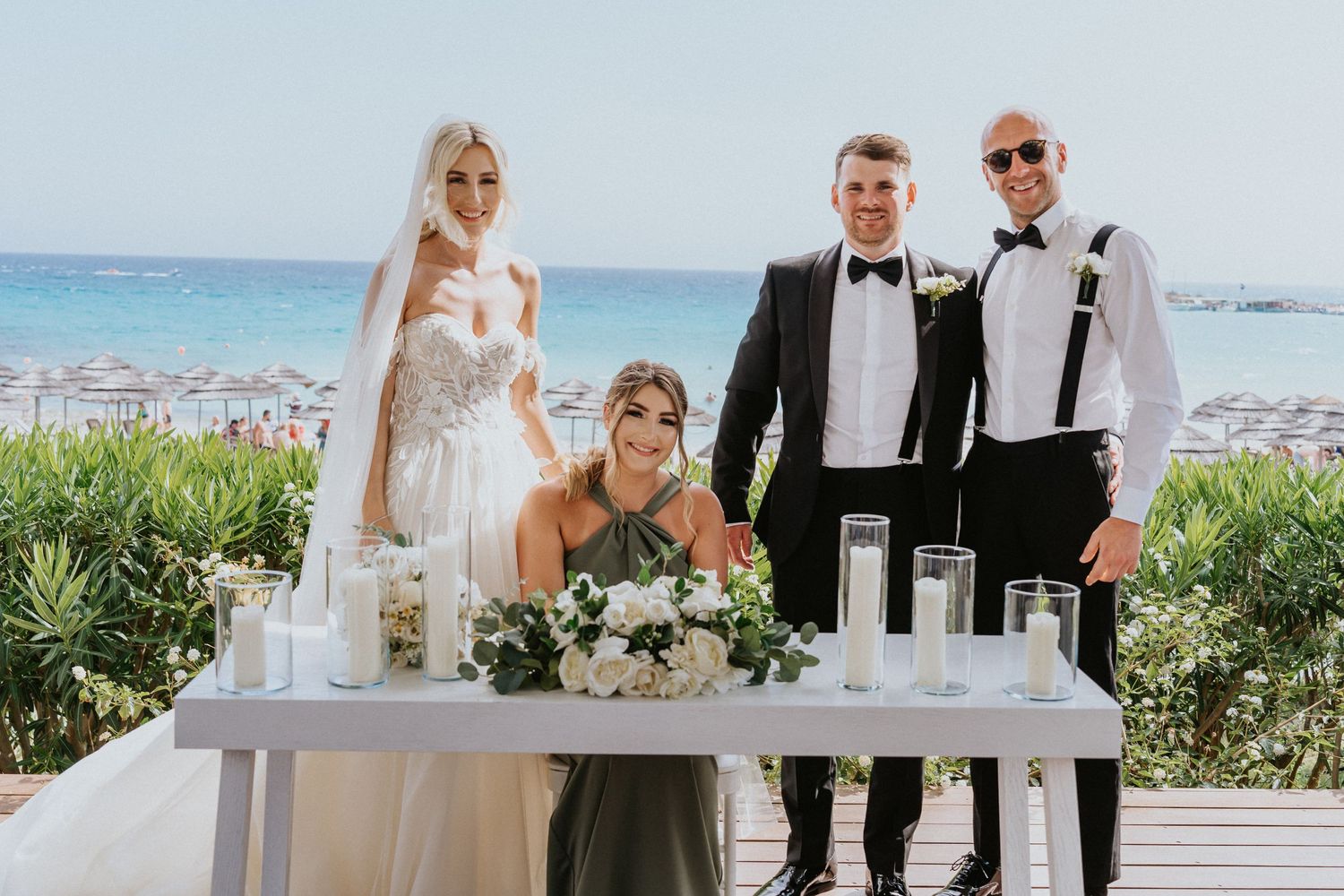 A small wedding party gathers around a signing table with ocean views in the background.