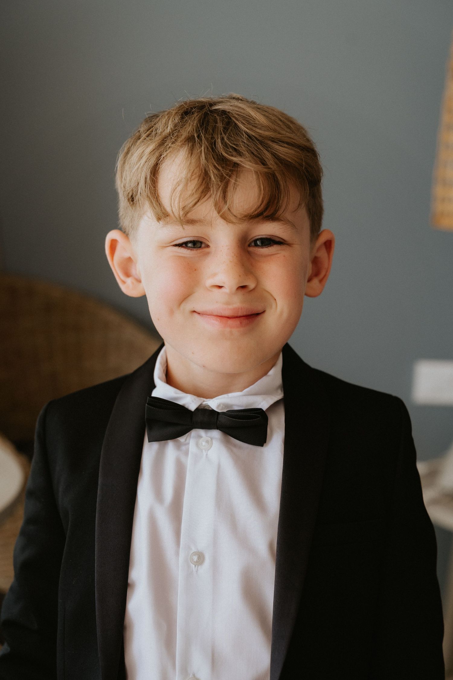 A young attendant in a black tuxedo and bowtie smiles at the camera.