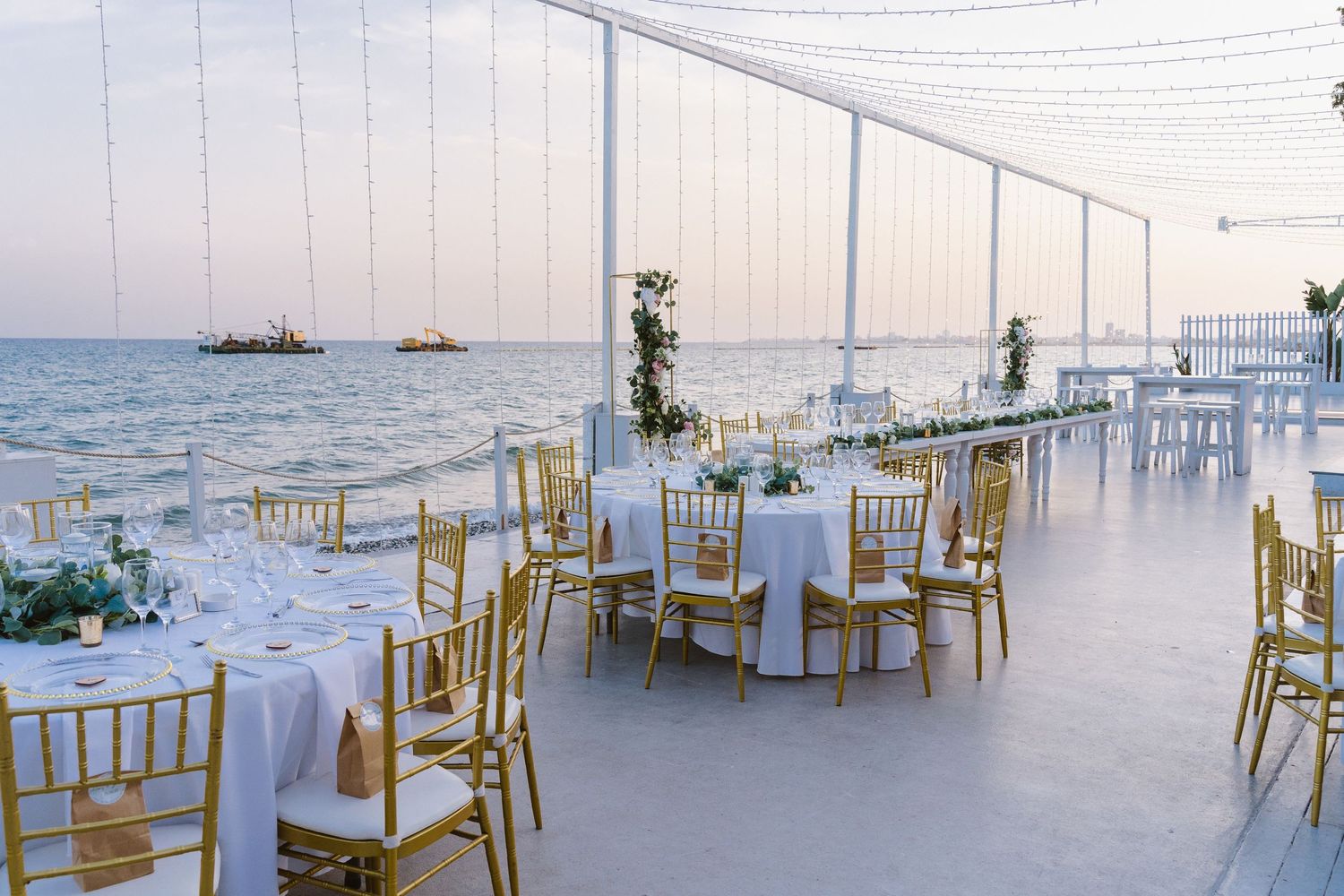 Seaside wedding reception venue with gold chiavari chairs and white linens overlooking the ocean.