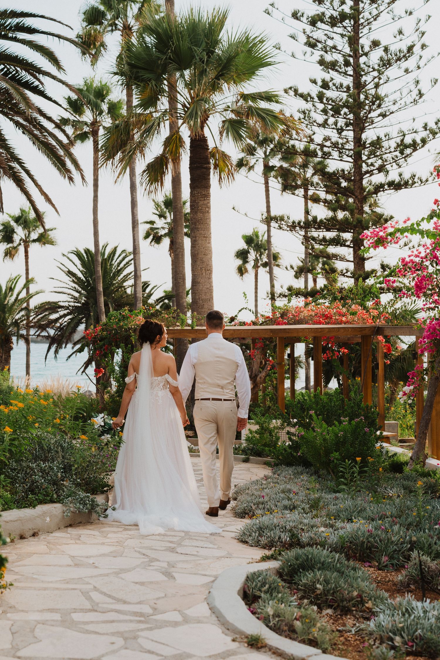 Couple walking down garden path surrounded by palm trees, succulents and bougainvillea in a tropical wedding setting.