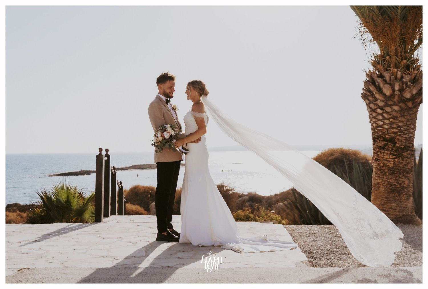 Windswept wedding veil photo with palm trees and ocean backdrop.