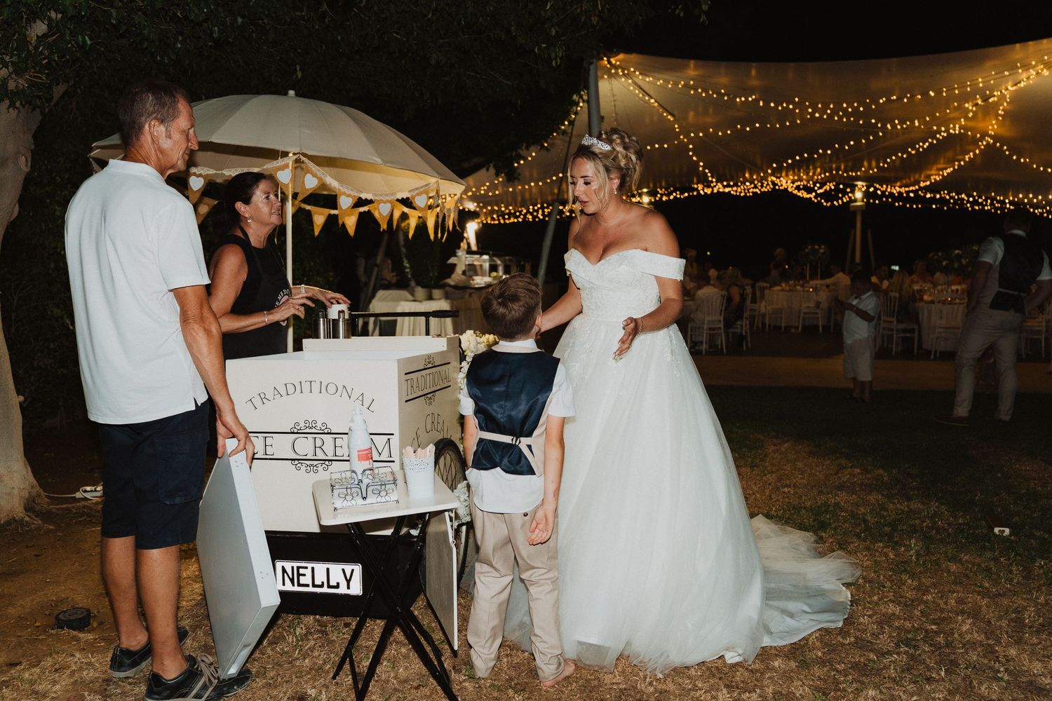 A wedding reception at night with string lights overhead as guests celebrate outdoors.