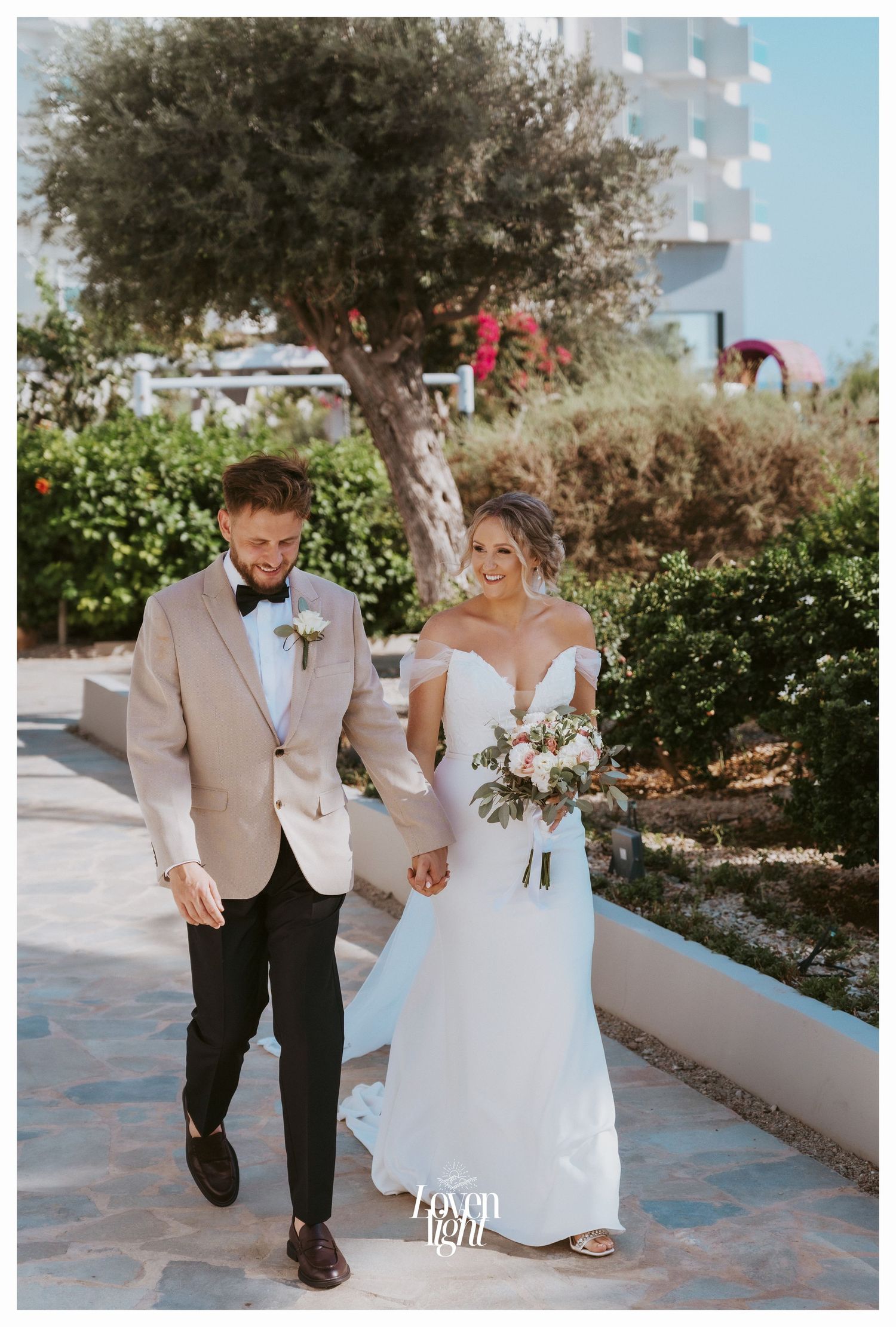 Newlyweds walking together along a stone pathway surrounded by lush garden landscaping.