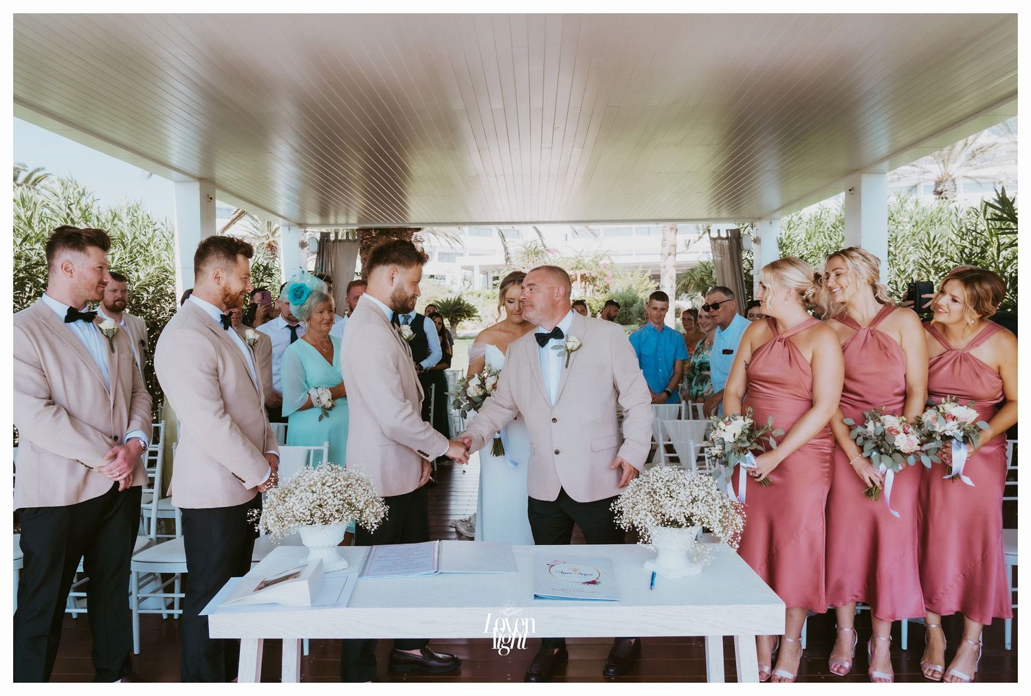 Wedding ceremony signing with bridal party in coral and beige gathered around white table.