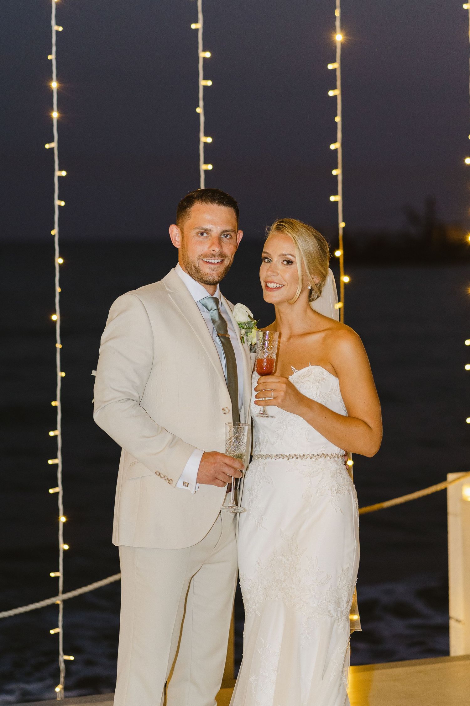 Couple poses for a romantic nighttime portrait with twinkling string lights in the background.
