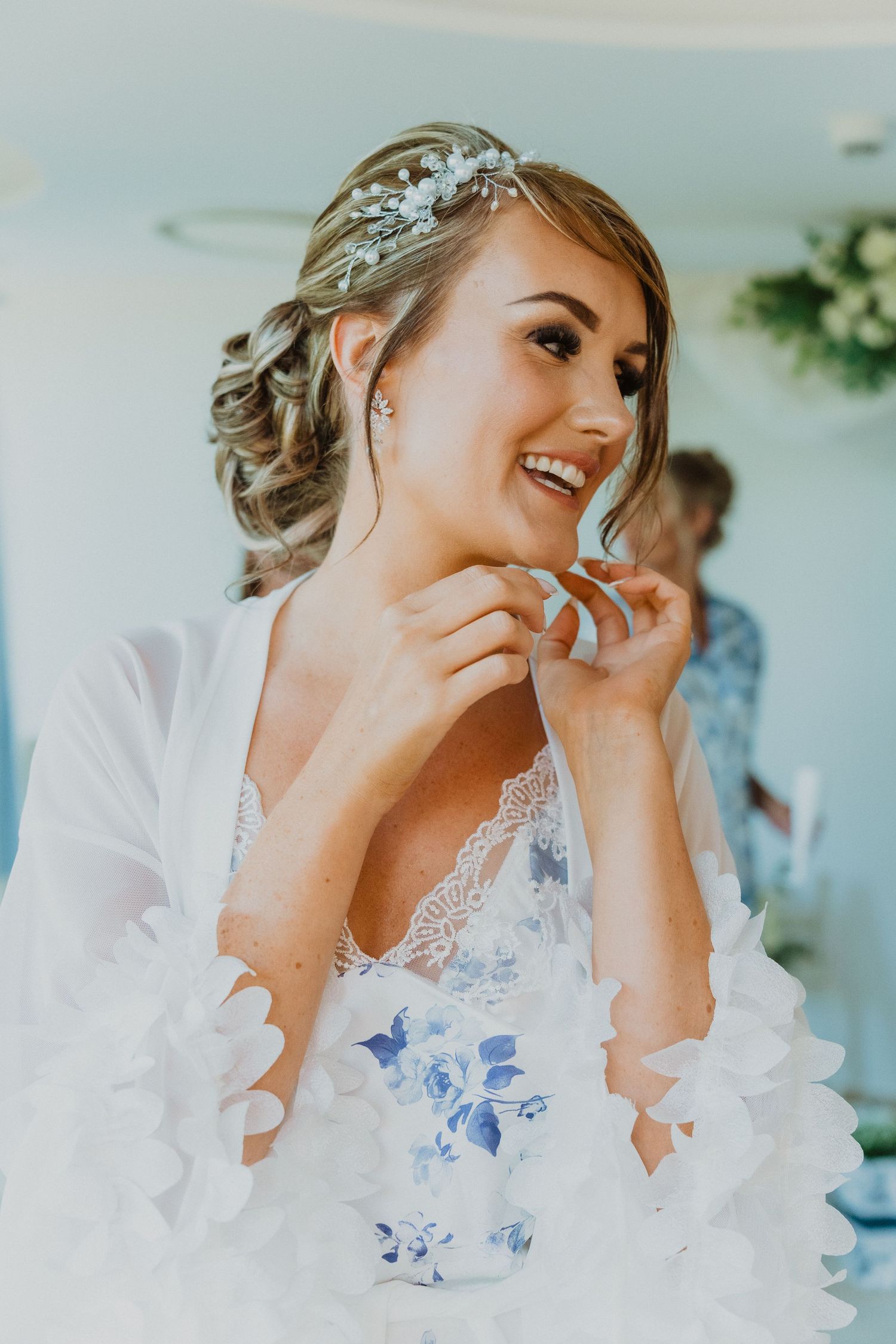 Person in white lace robe laughs joyfully during wedding preparations.