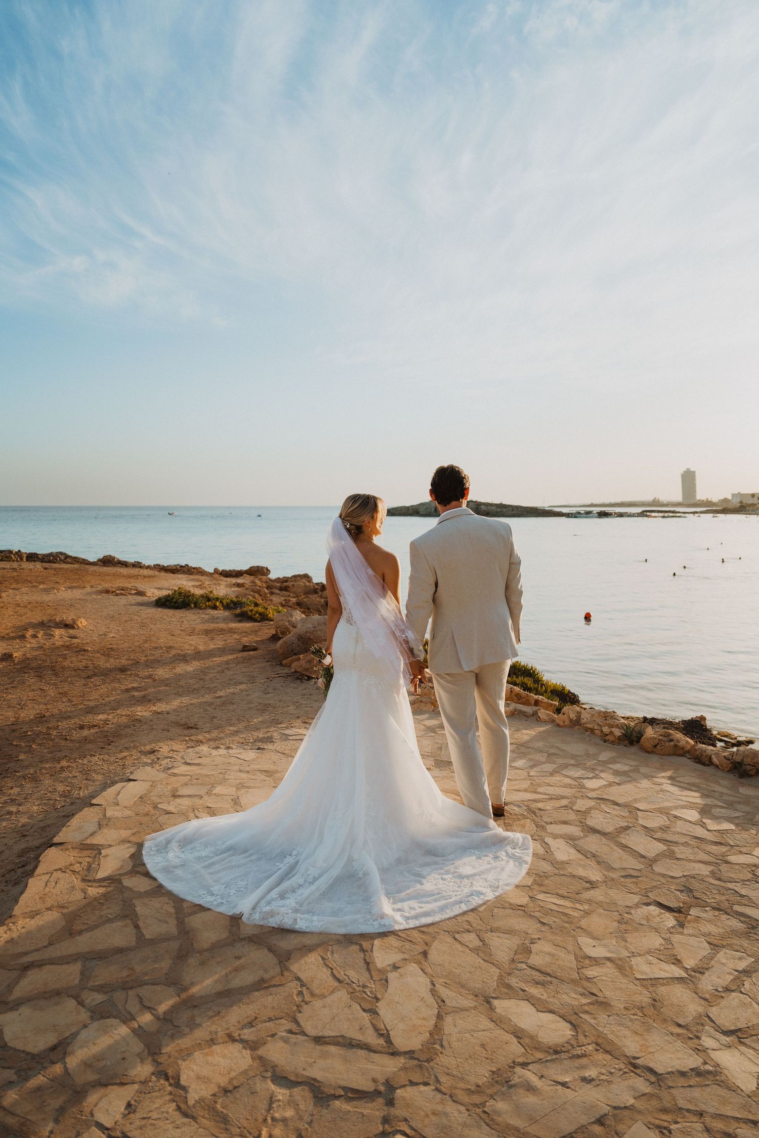 Wedding couple standing on stone pathway overlooking serene ocean view.