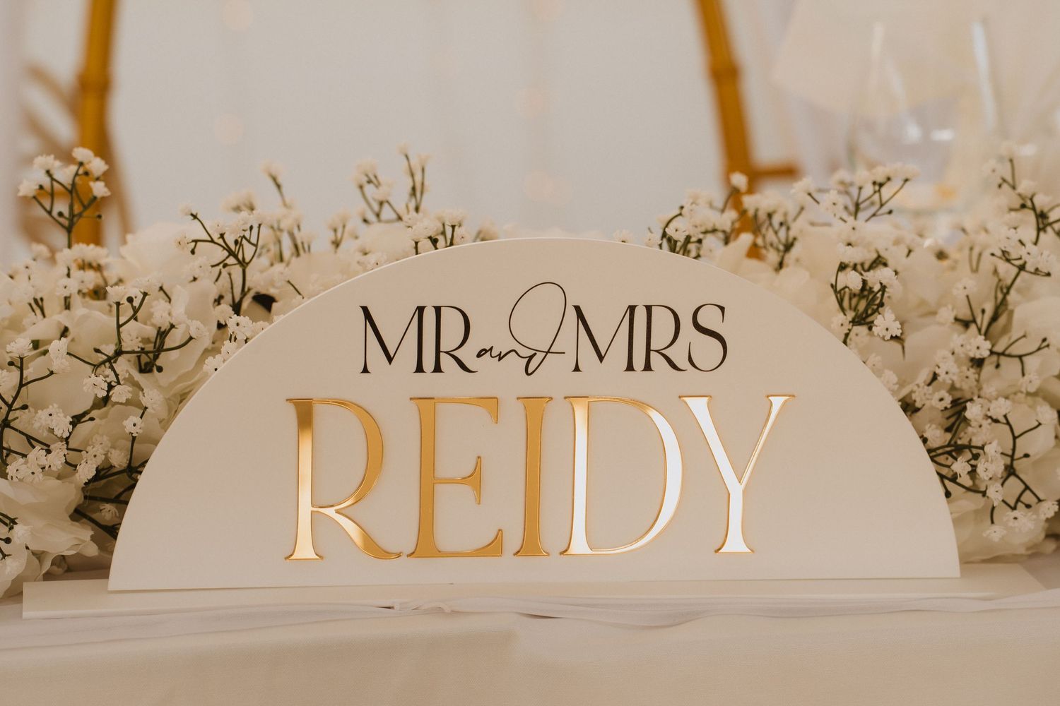 Elegant illuminated Mr and Mrs Reidy wedding sign surrounded by white baby's breath floral arrangements.