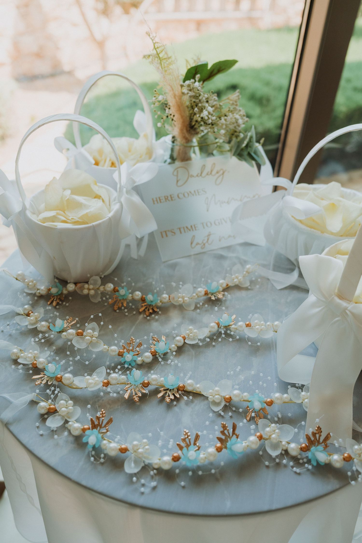Elegant wedding table with pearl and turquoise floral garlands, white flower girl baskets, and a daddy sign for the ceremony.