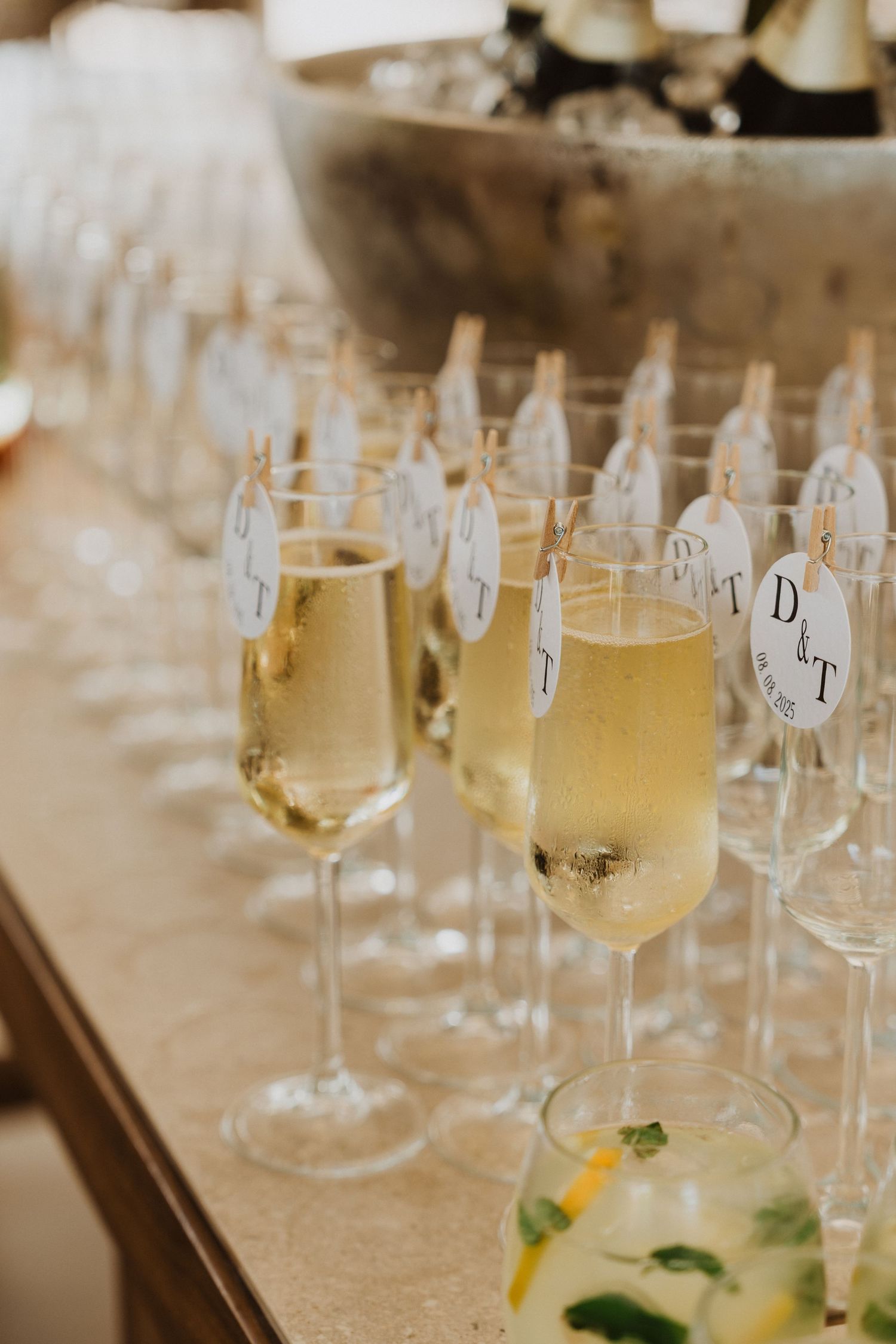 Multiple glasses of white wine arranged in rows on a table with small paper labels for wine tasting.