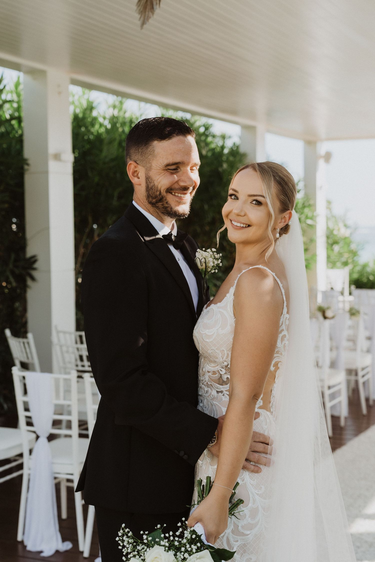 A bride and groom share intimate moments on their wedding day under a covered porch with white columns.