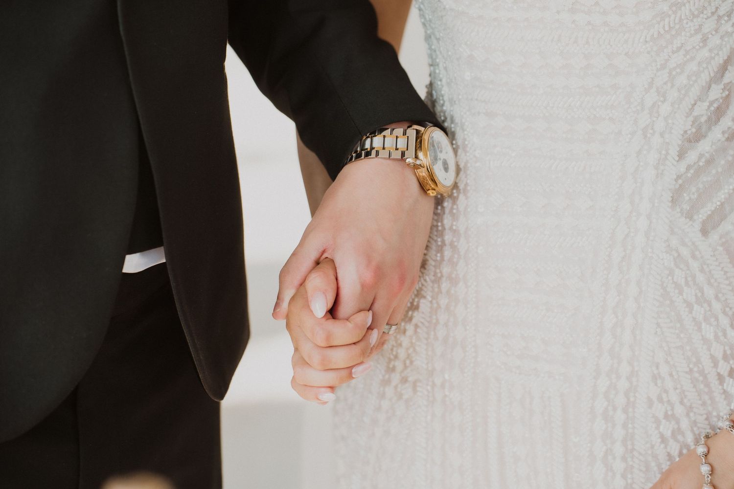 Bride and groom holding hands, groom wearing gold Rolex watch, during wedding ceremony.