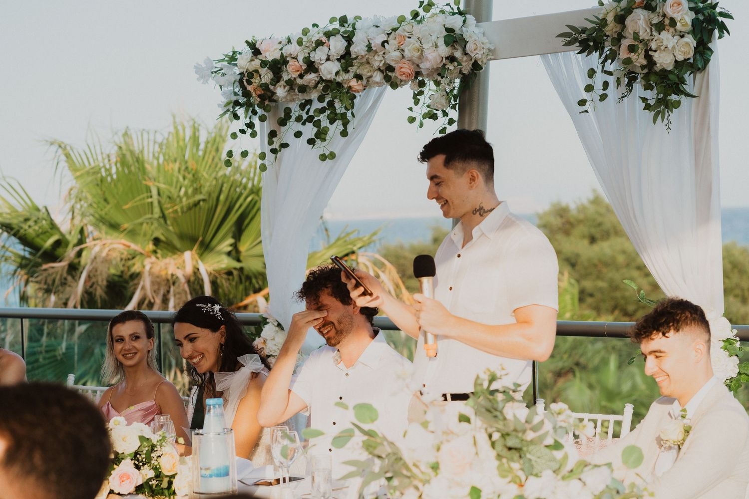 Wedding guests enjoying emotional speeches during outdoor reception by the ocean.