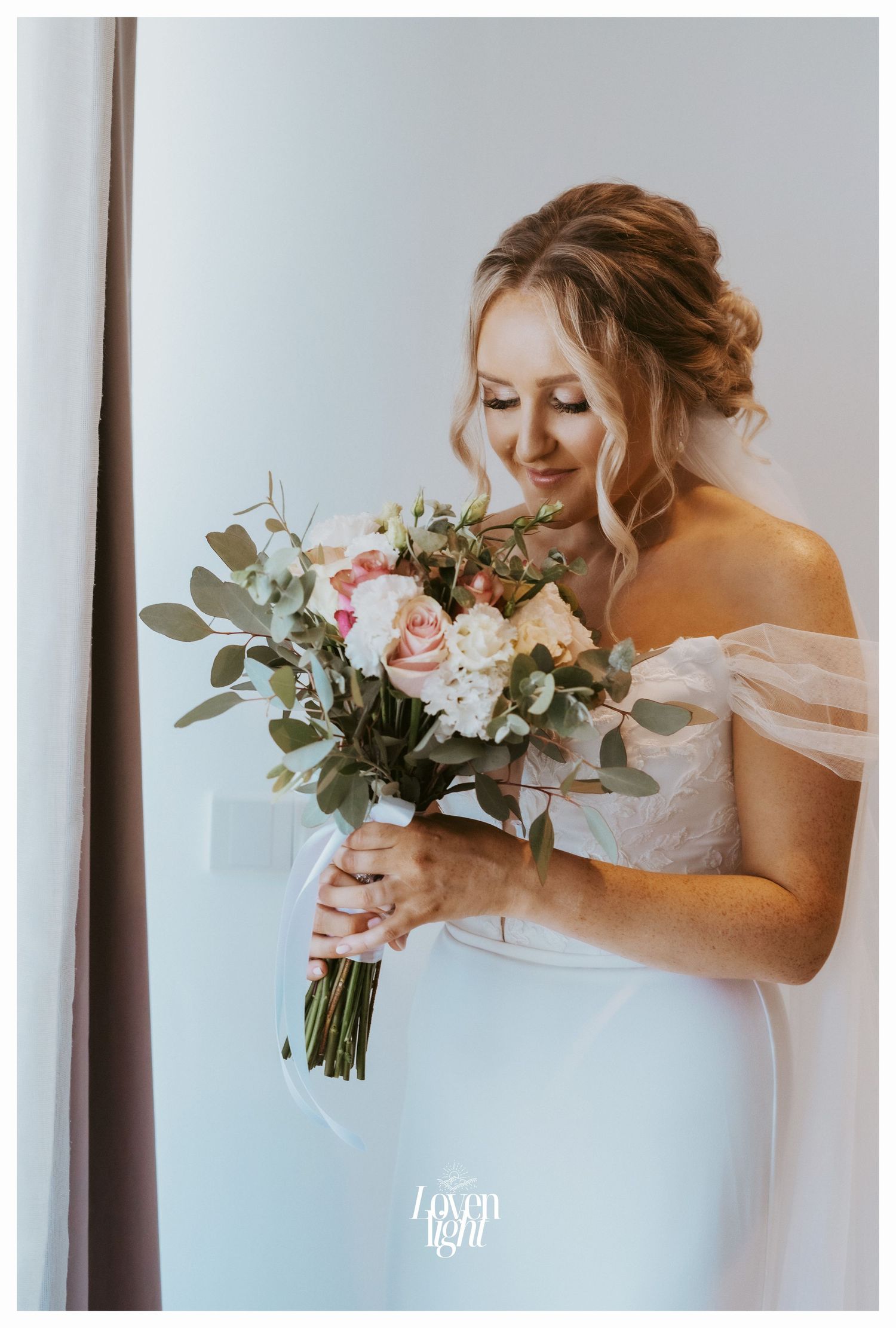 Bride holding floral bouquet in elegant off-shoulder wedding dress.