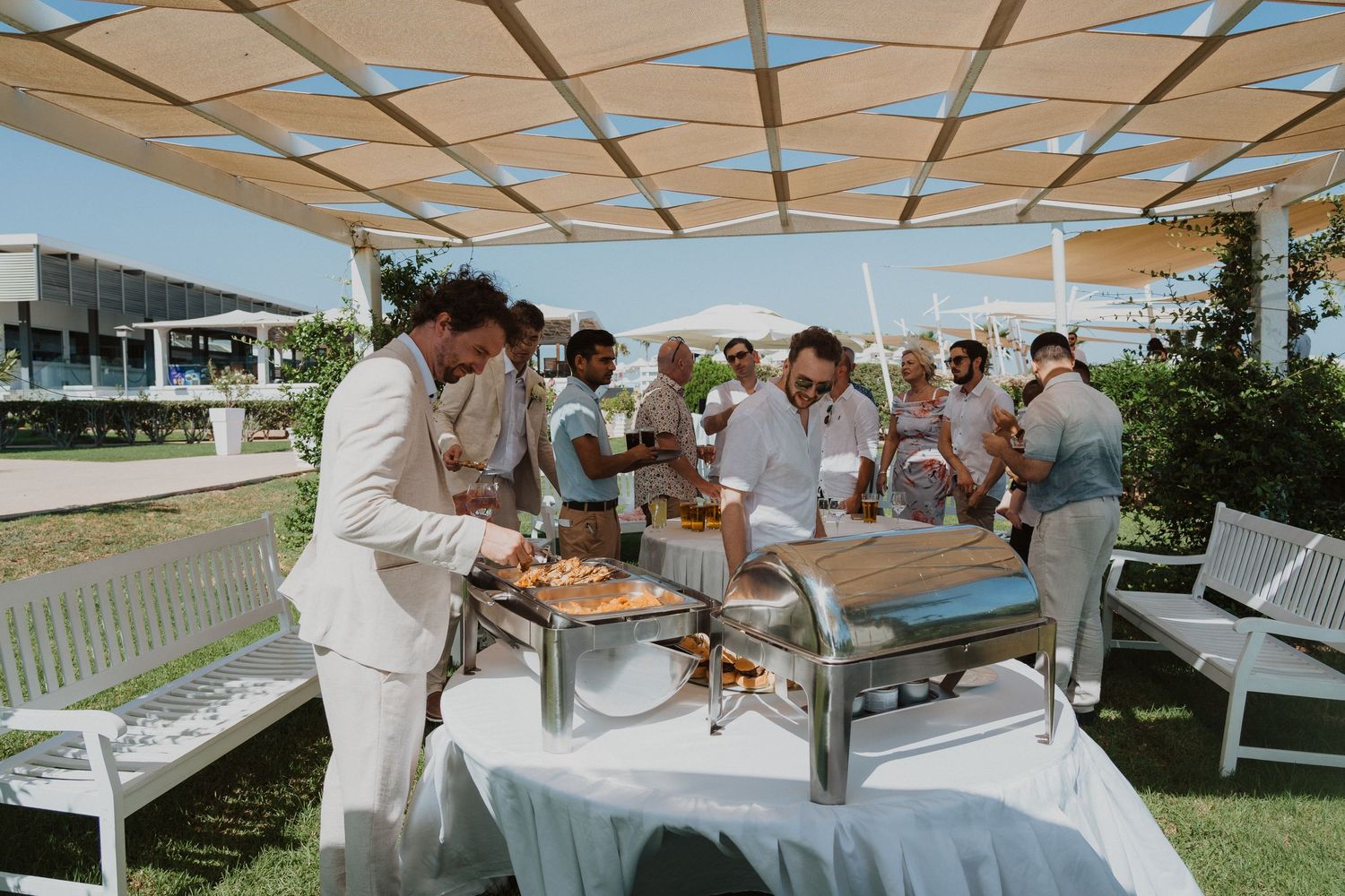 Wedding reception buffet setup with guests serving food under outdoor canopy.