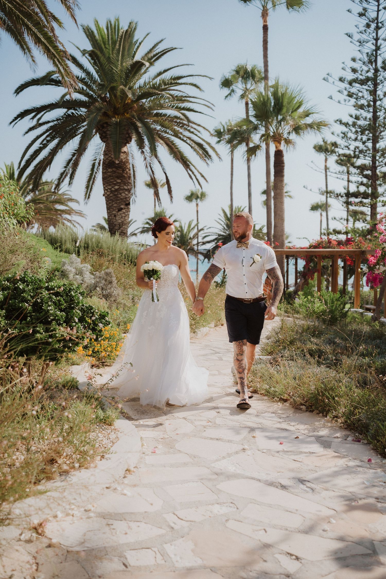 Couple walking hand in hand on stone path surrounded by tropical palm trees.