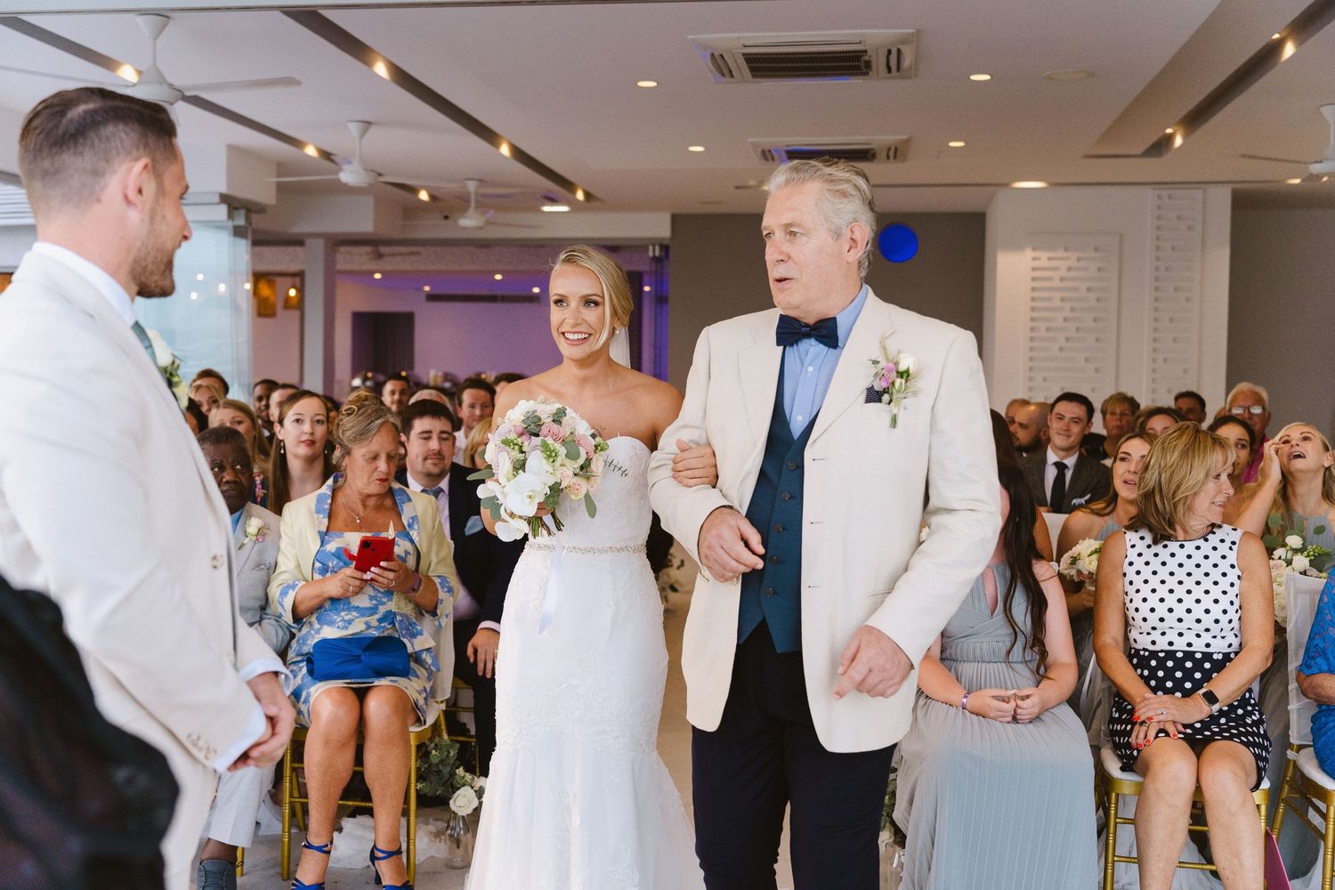 Elegant indoor wedding ceremony with guests watching as couple stands before officiant in white decor.