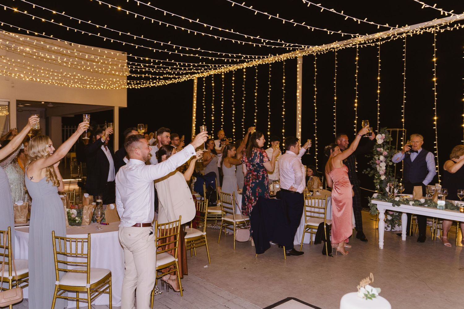 Wedding guests dance and celebrate under glittering string lights at an evening reception.