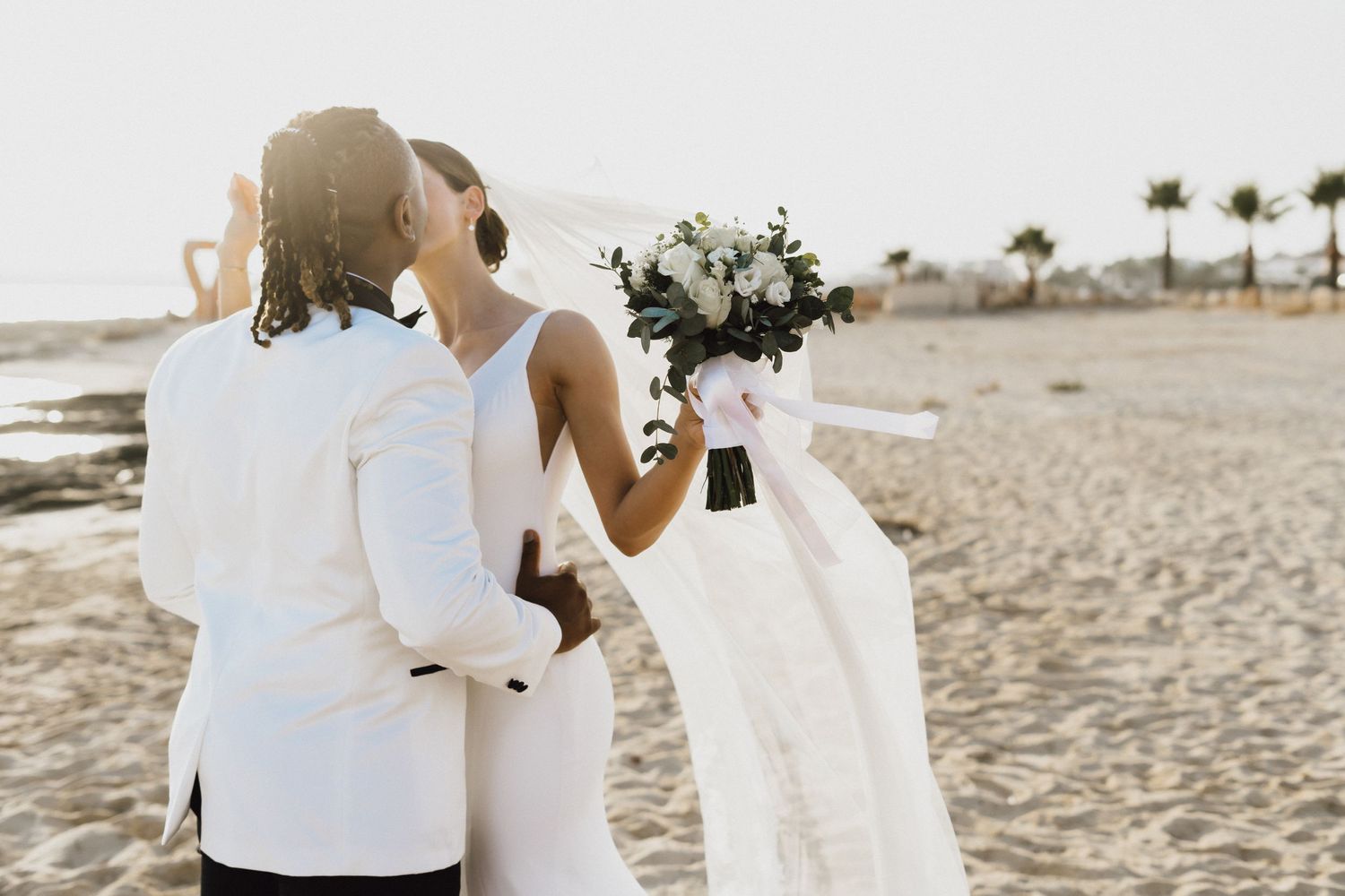 Newlyweds share an intimate moment on the beach with white floral bouquet.
