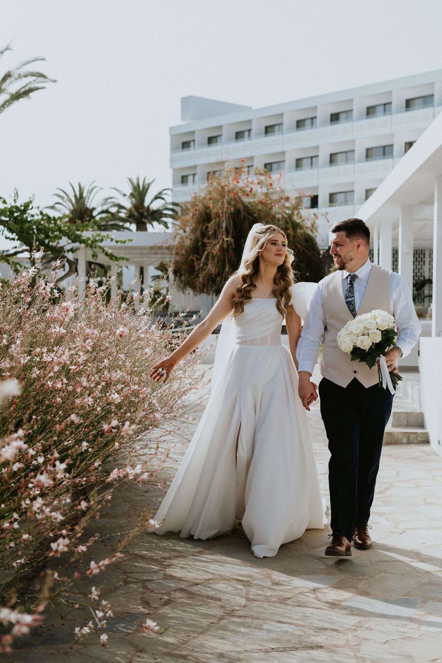 Couple strolls along resort pathway with blooming cherry blossoms and palm trees.