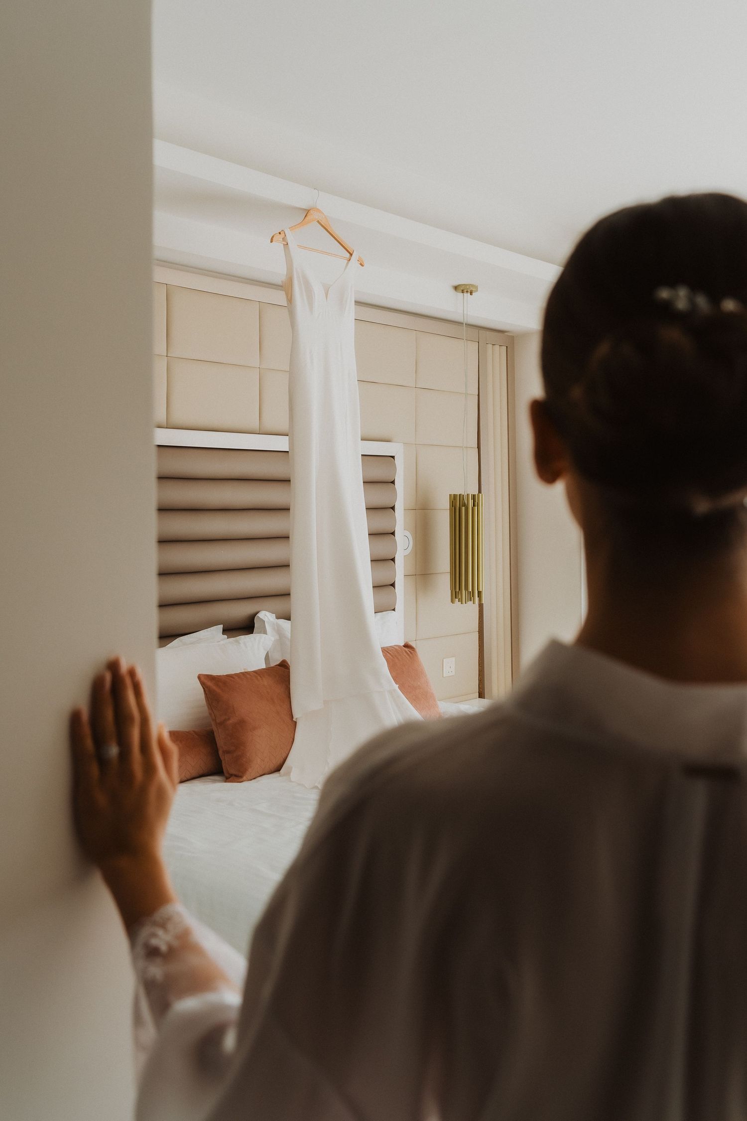 An elegant white wedding dress hangs in a modern hotel room.