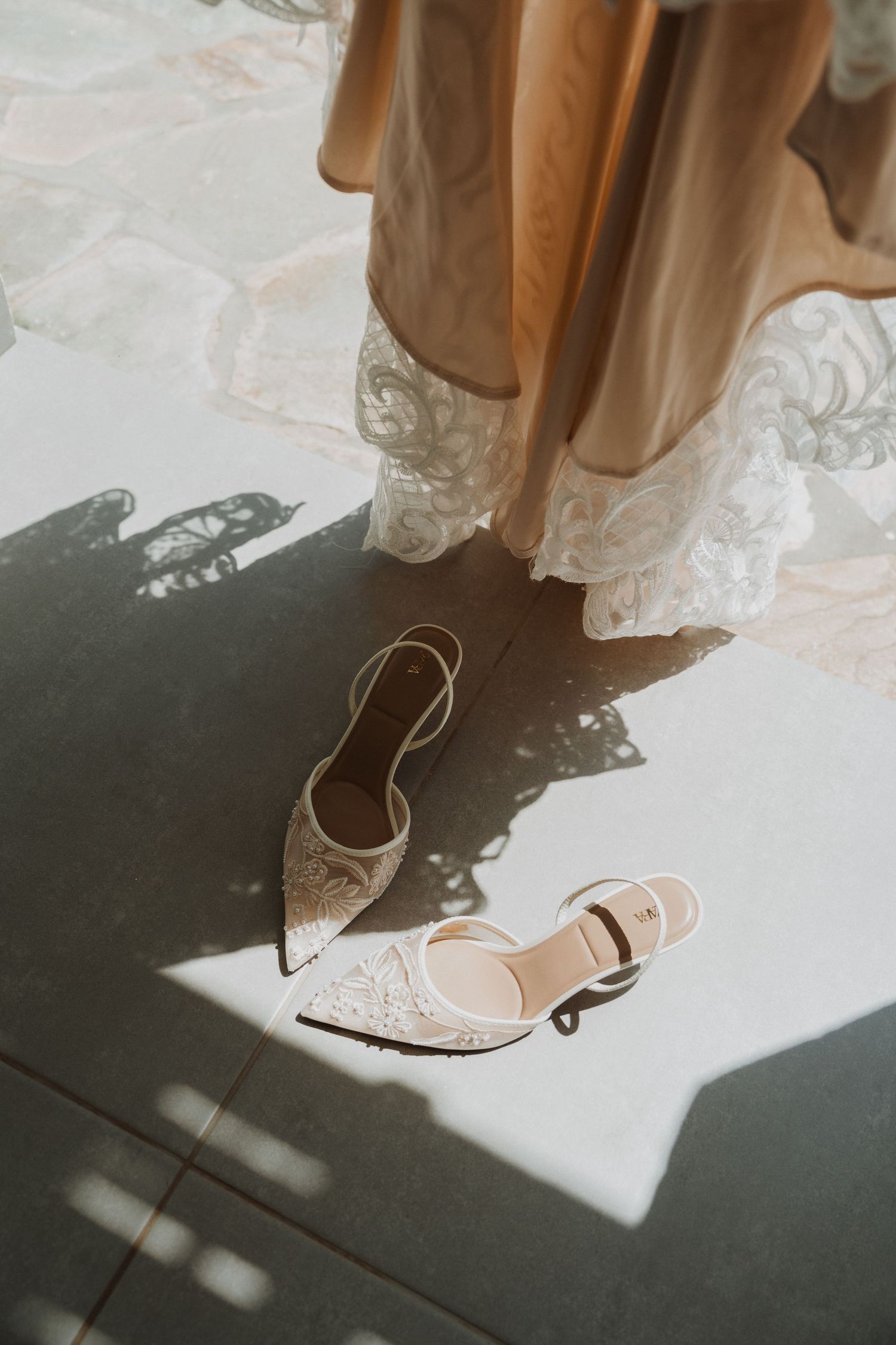 Elegant bridal shoes with delicate lace details and pointed toes cast dramatic shadows on a light floor.
