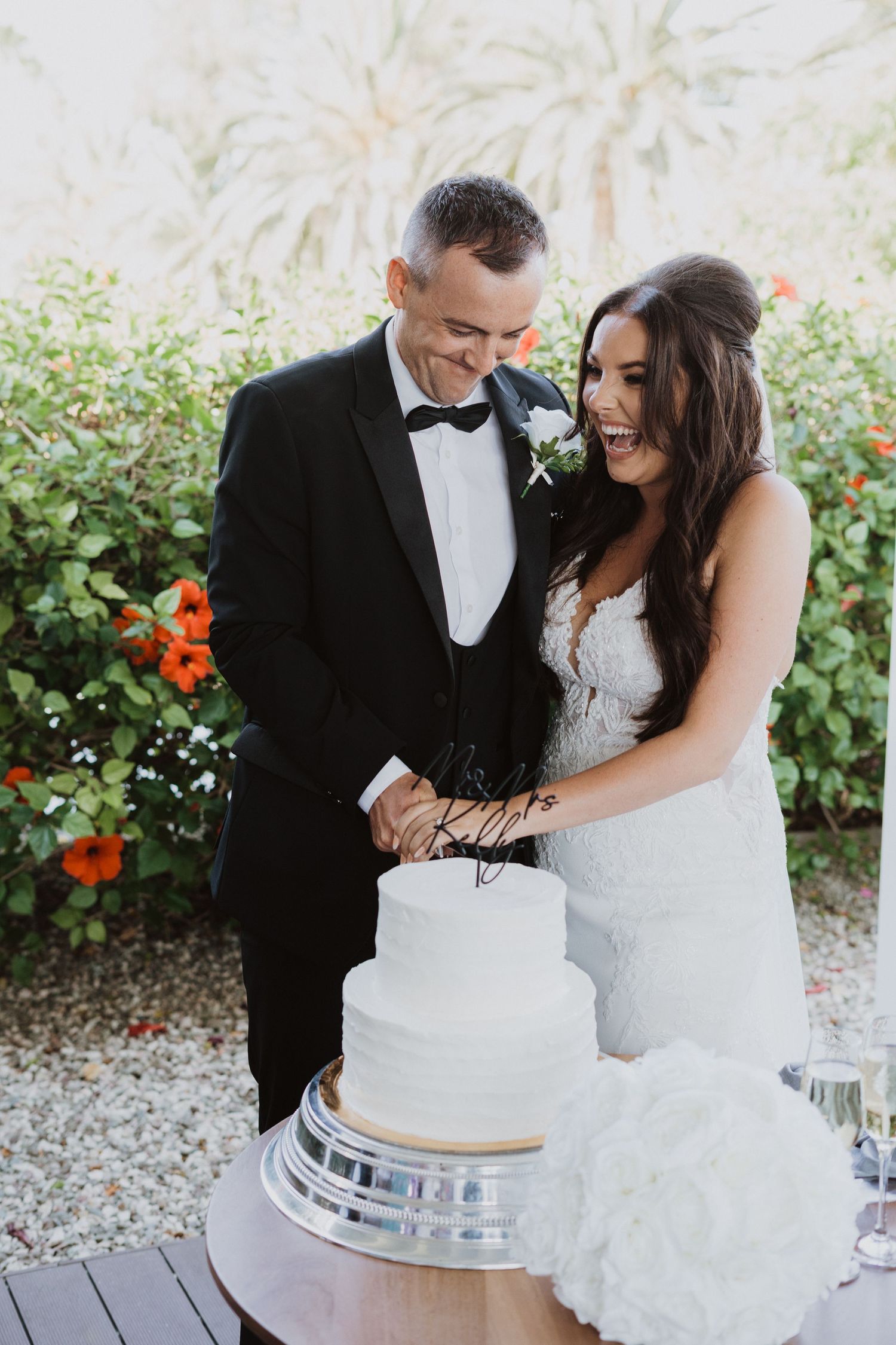 A couple shares a sweet moment while cutting their elegant white wedding cake.
