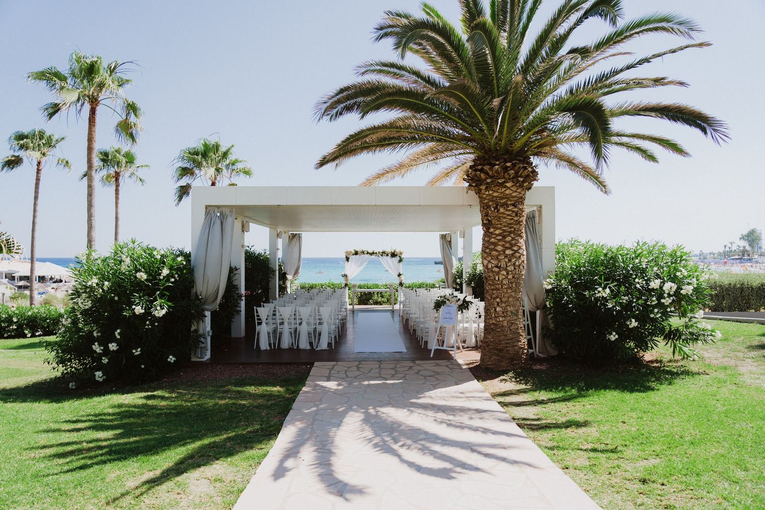 Palm tree lined pathway leading to a white wedding venue entrance.