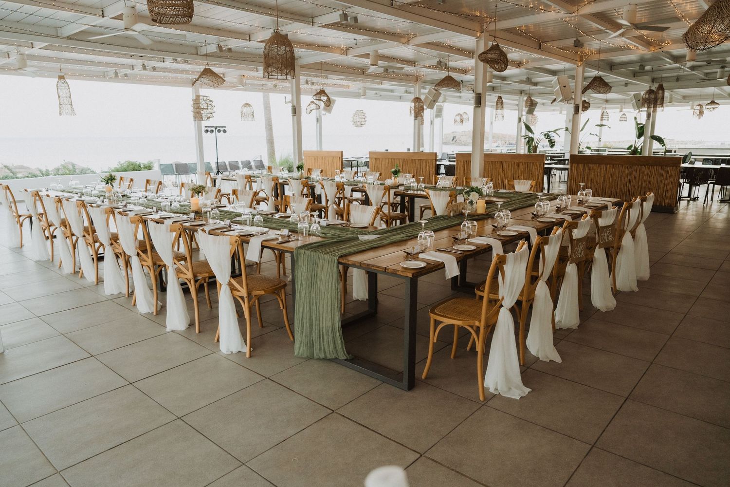 Wedding reception hall setup with white chair covers and elegant table arrangements in natural light.