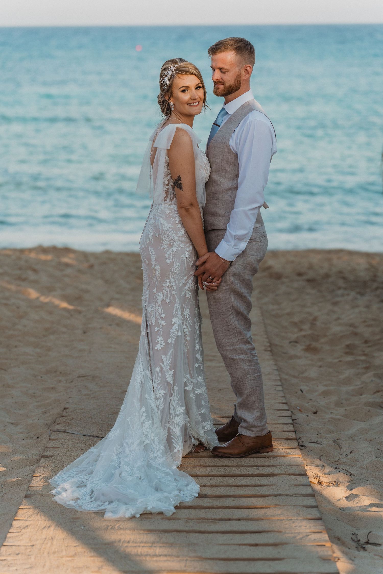 Wedding couple poses on wooden beach walkway at sunset.