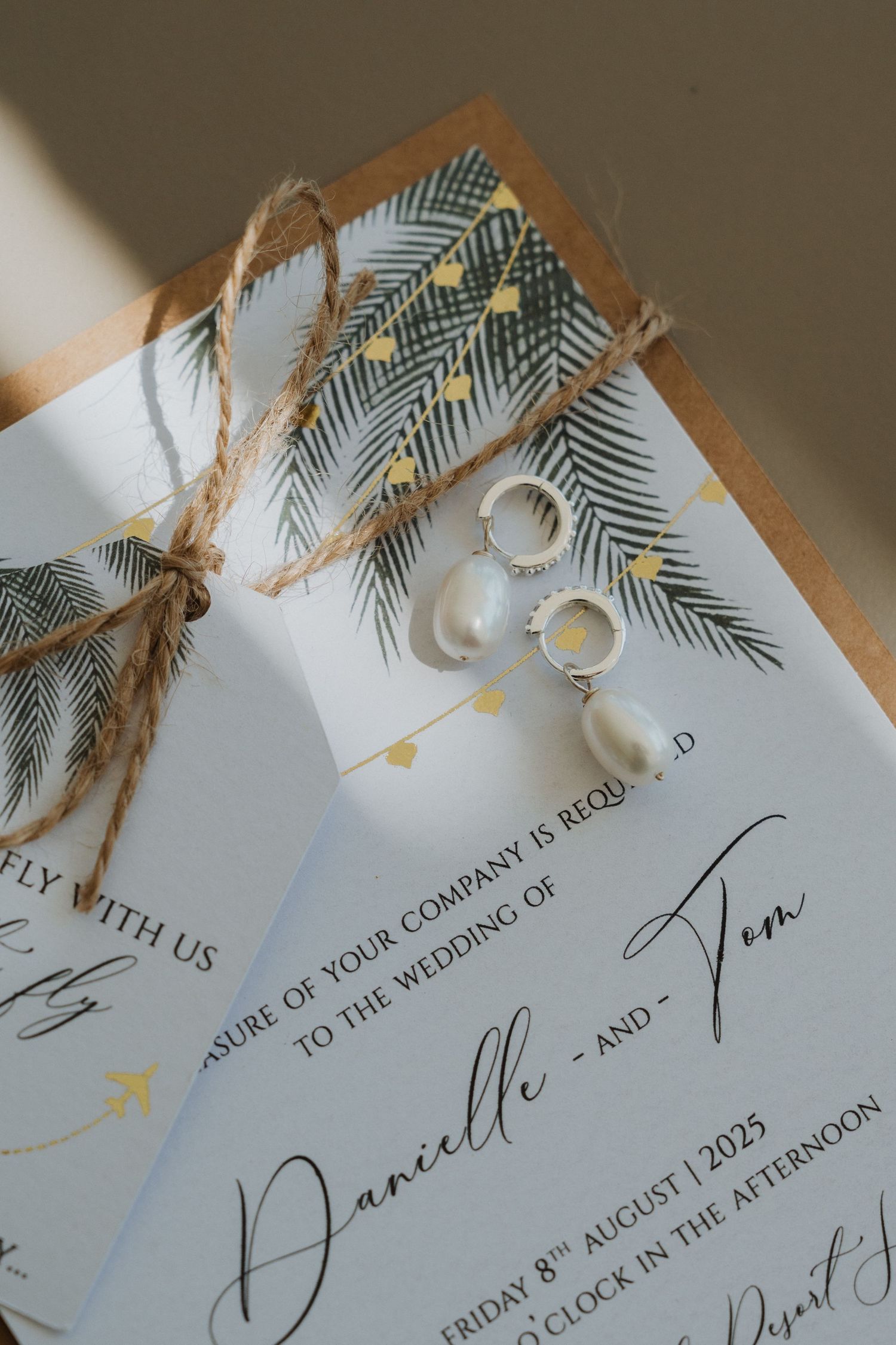 Wedding invitation cards with tropical palm leaf designs and twine details displayed in a fanned arrangement.