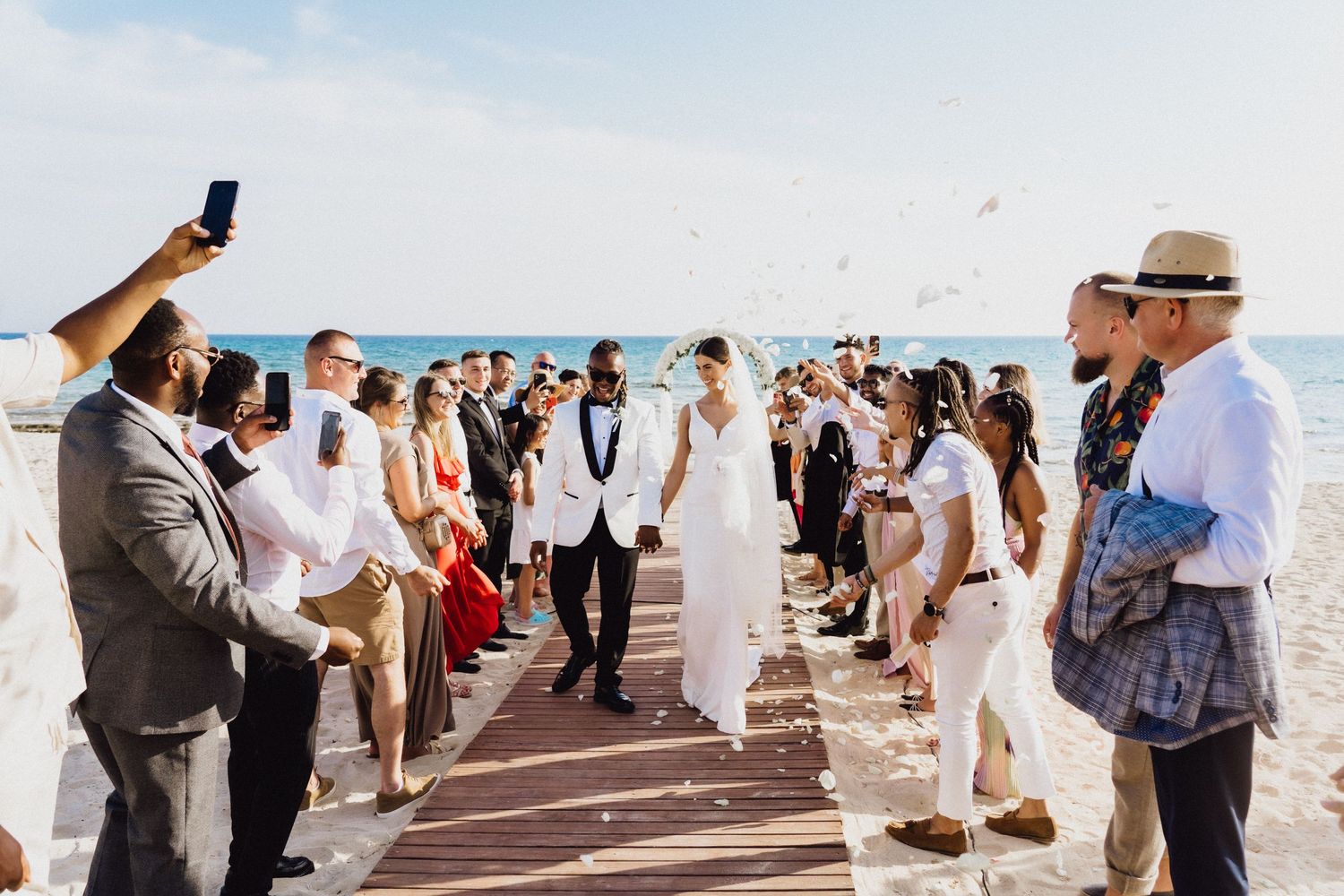 Wedding celebration on oceanfront boardwalk with guests taking photos.